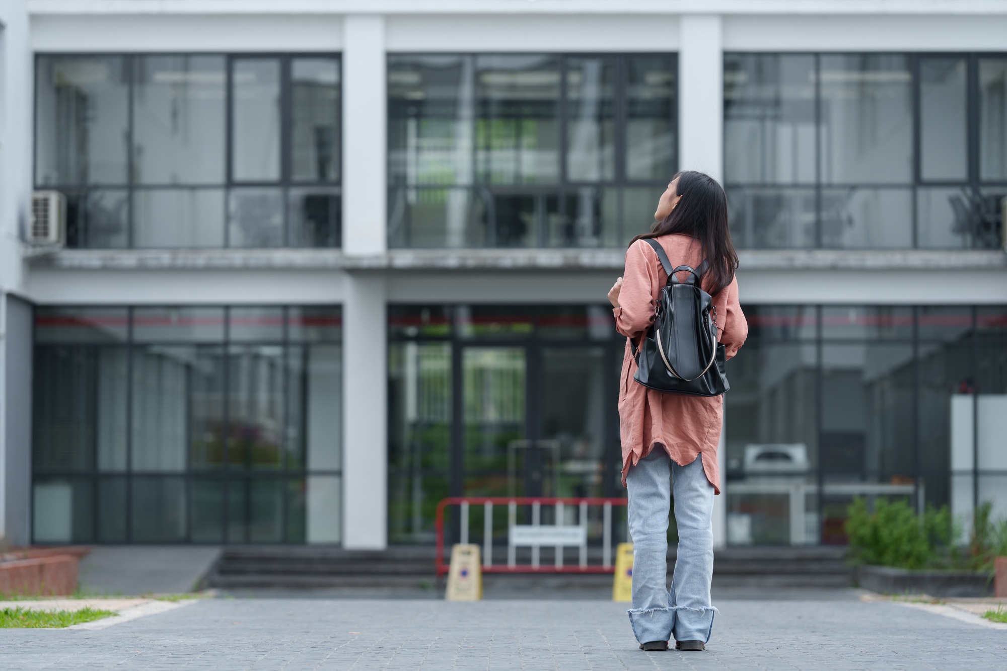 Young female student wearing backpack standing in front of university building contemplating future