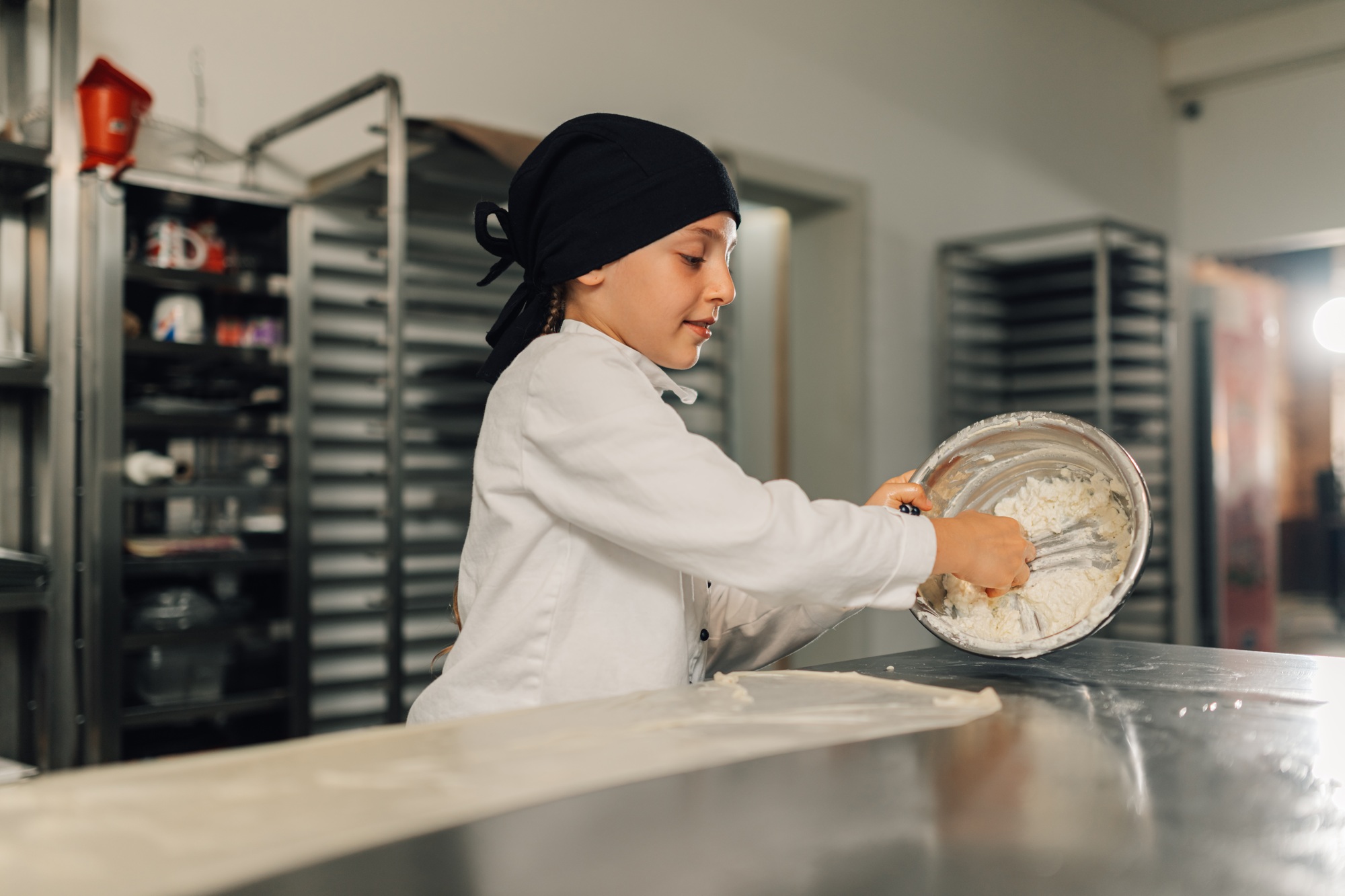 Young girl chef mixing flour in a bowl in professional kitchen setting.