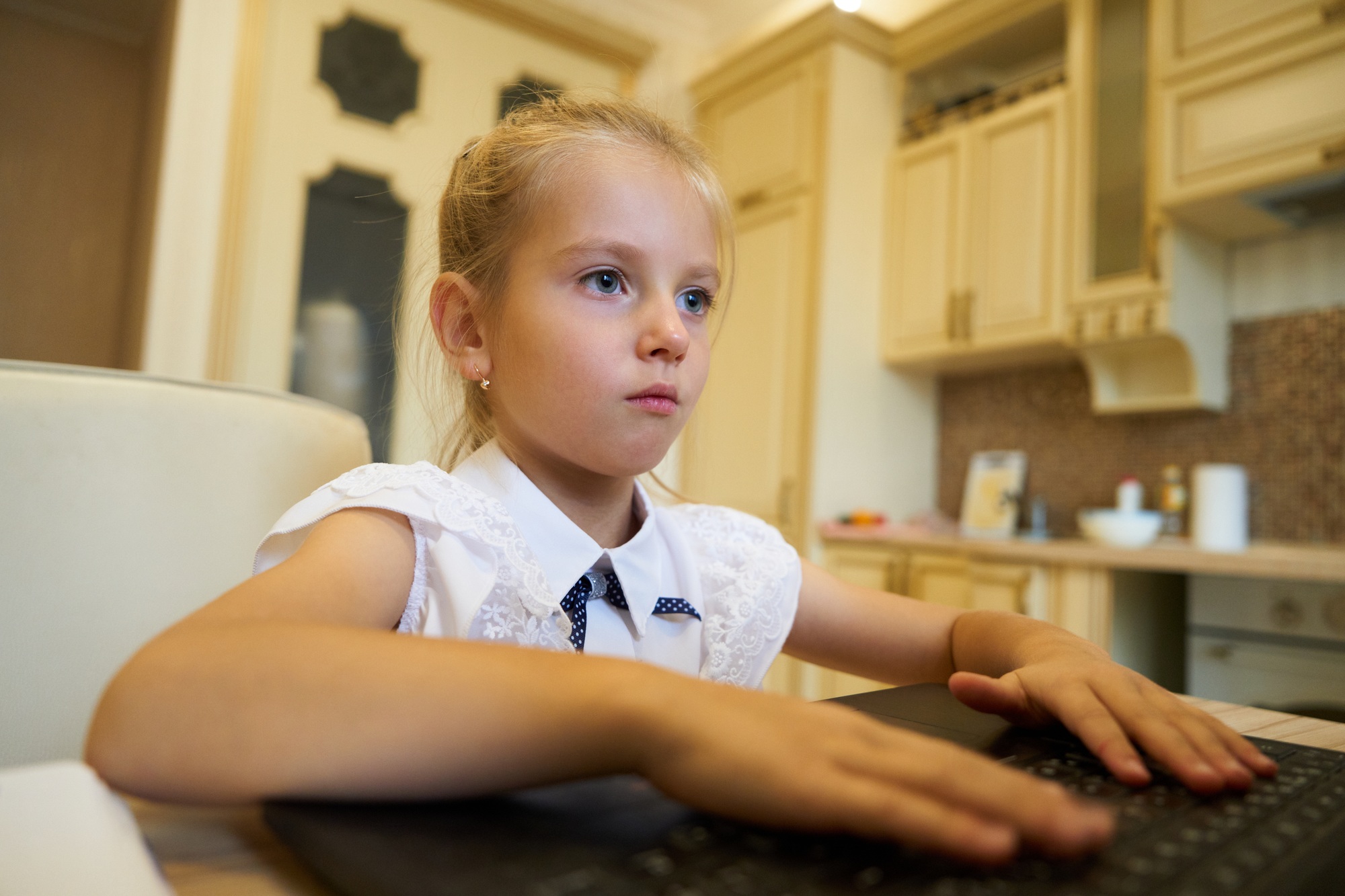 Young girl concentrating while typing on a laptop in a cozy kitchen setting