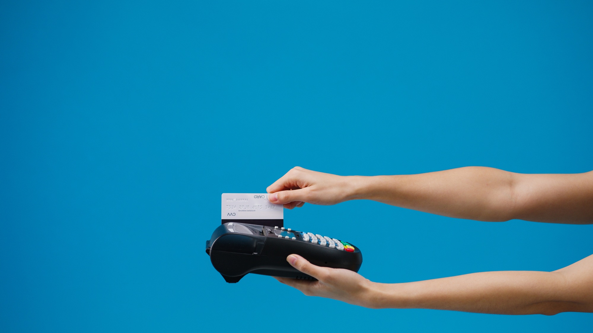 Young girl using credit card into credit card machine or pos terminal blue background in studio.