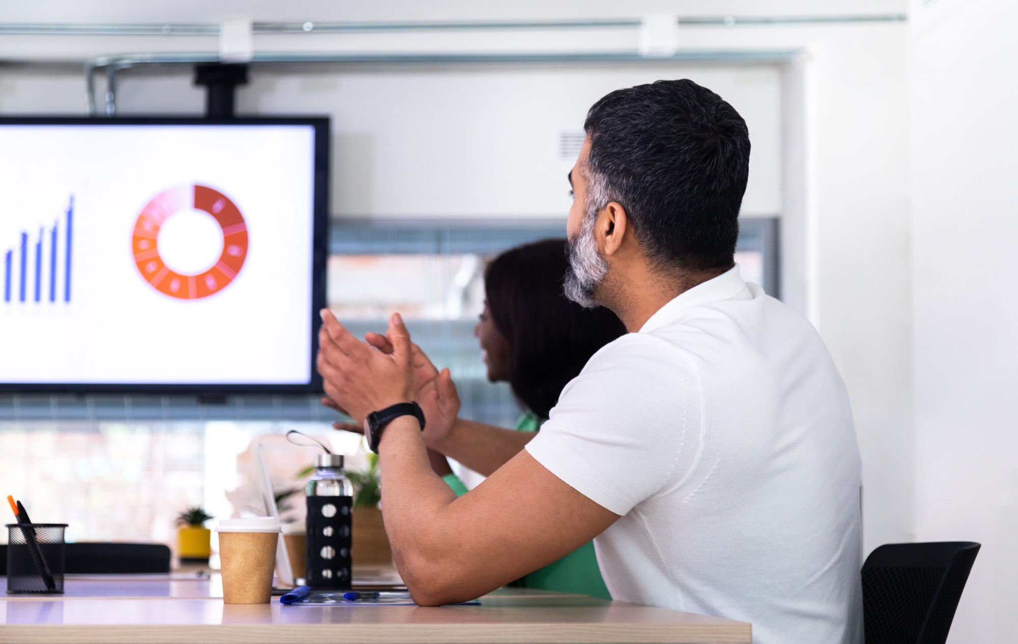 Young indian man applauding during business meeting celebrating great company sales with coworkers.