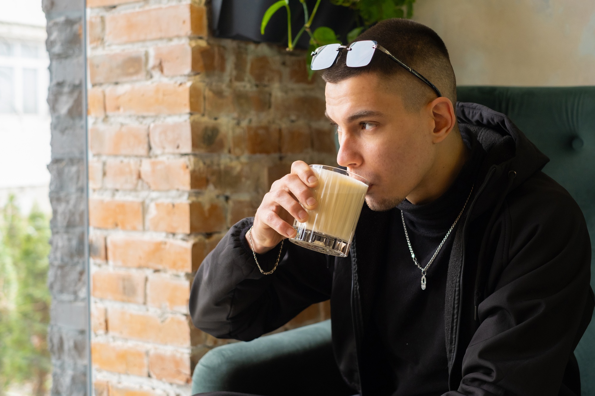 Young man enjoying a cold drink in a modern cafe with stylish decor and indoor plants