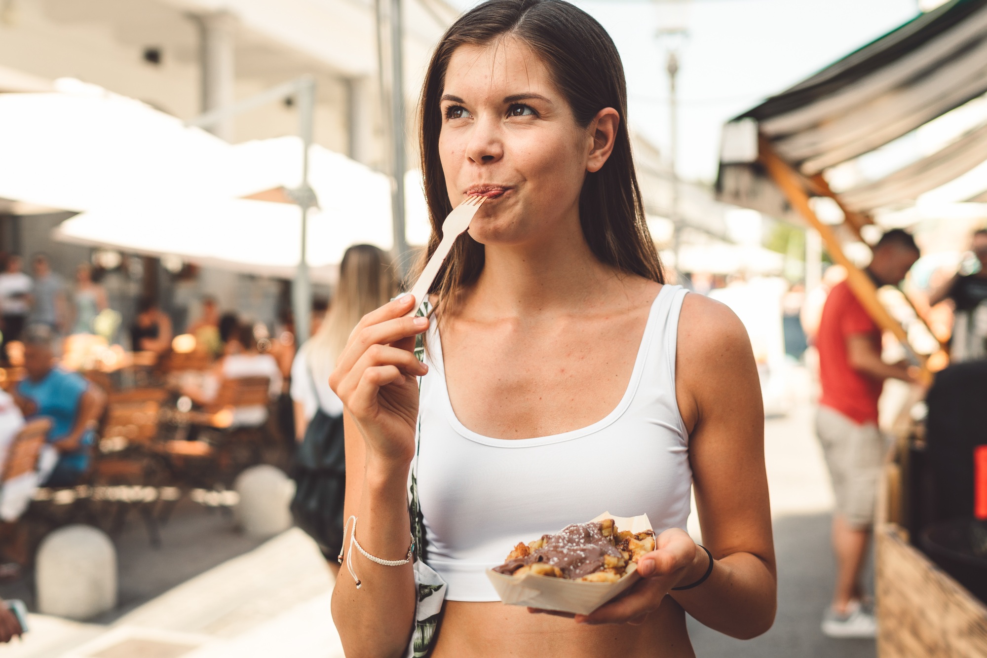 Young woman enjoying her dessert at the food market, licking the fork and smiling