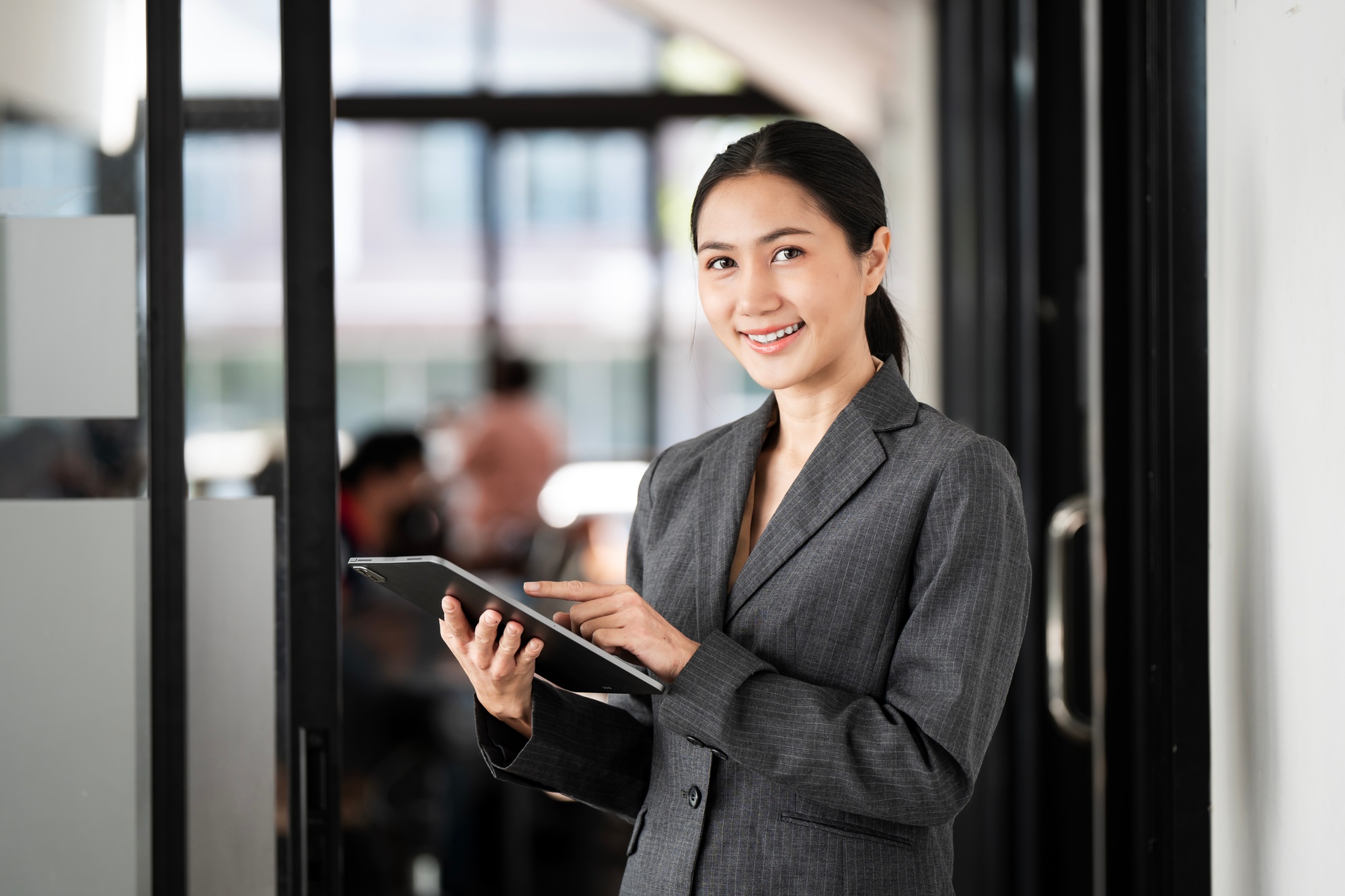 Young woman in business attire efficiently works on a tablet in a modern office.