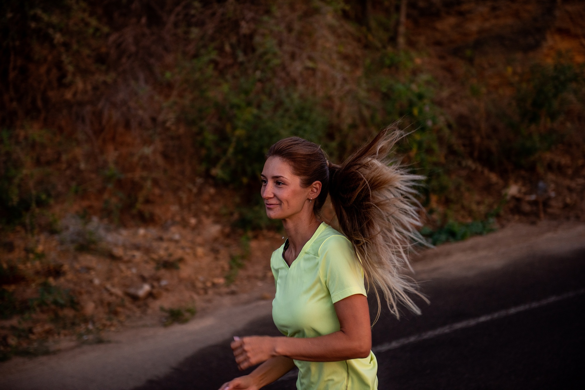 Young woman in sportswear is jogging early in morning on green track at sunrise. Pursuit of goals
