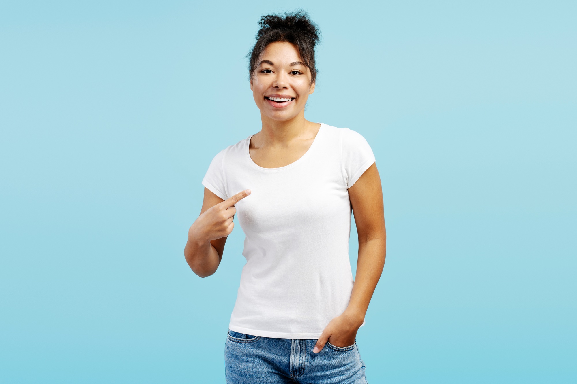 Young woman pointing at her white t shirt on blue background