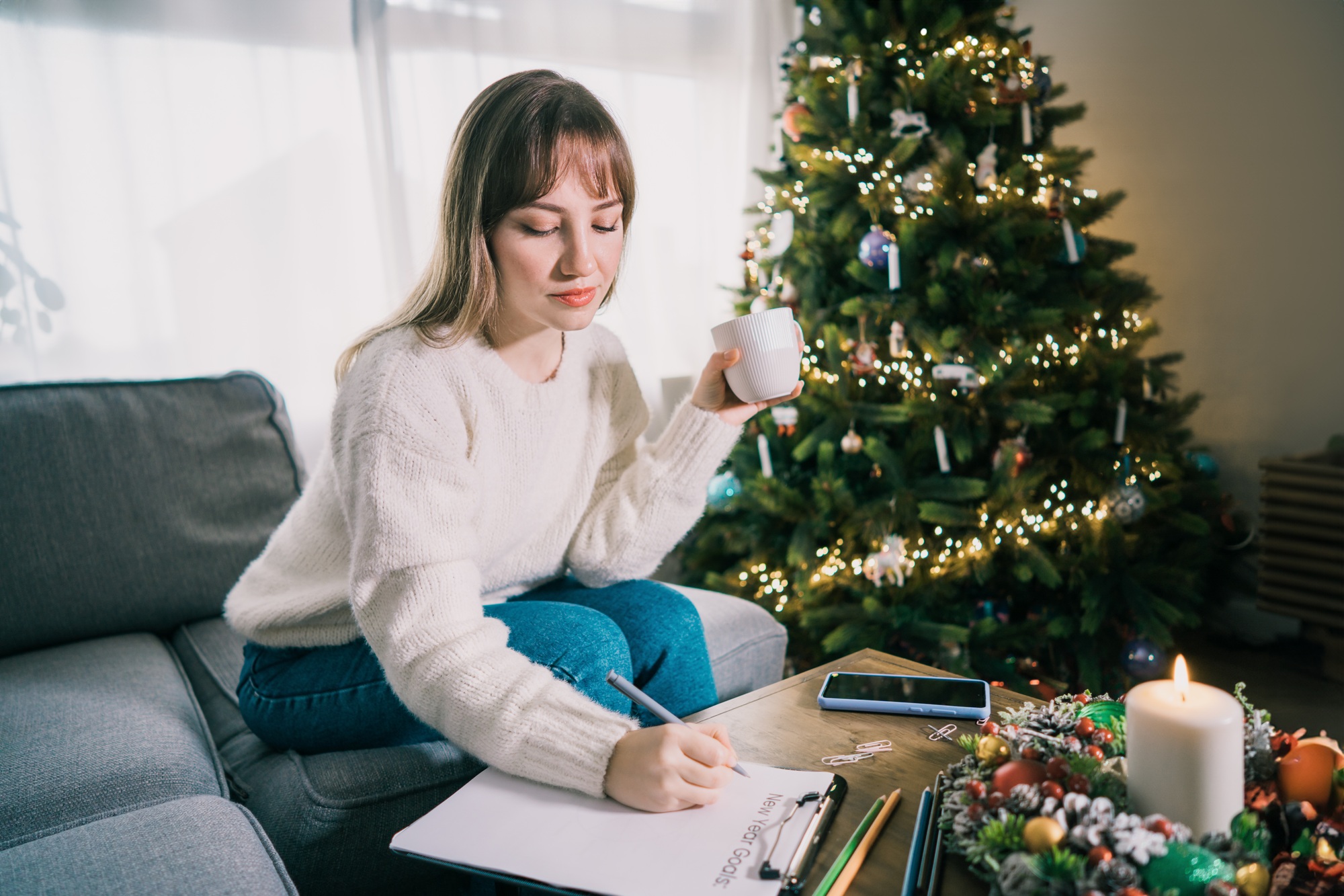 Young Woman with cup is hand writing New year's goals on note paper in new year day. New year goals