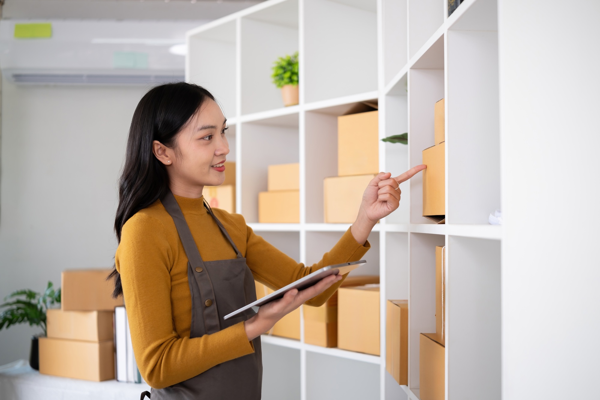 Young woman working in warehouse with packages using tablet for inventory management