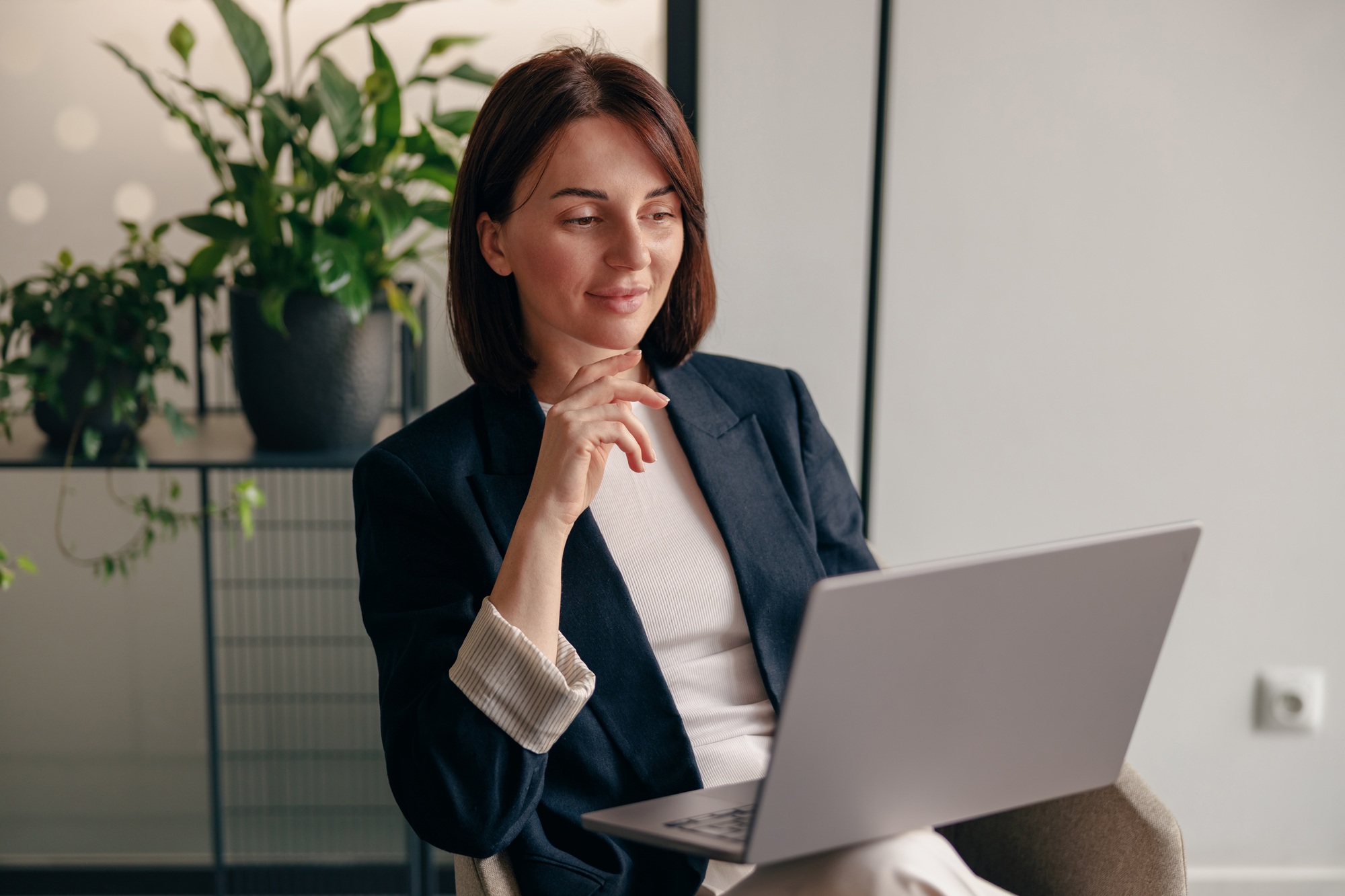 A businesswoman in a modern office setting is concentrating on her tasks using a laptop