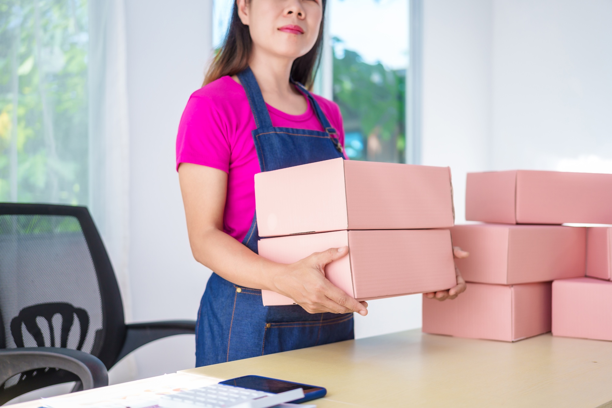 A woman in overalls sells products online, inspects parcels, takes customer orders, works at a desk
