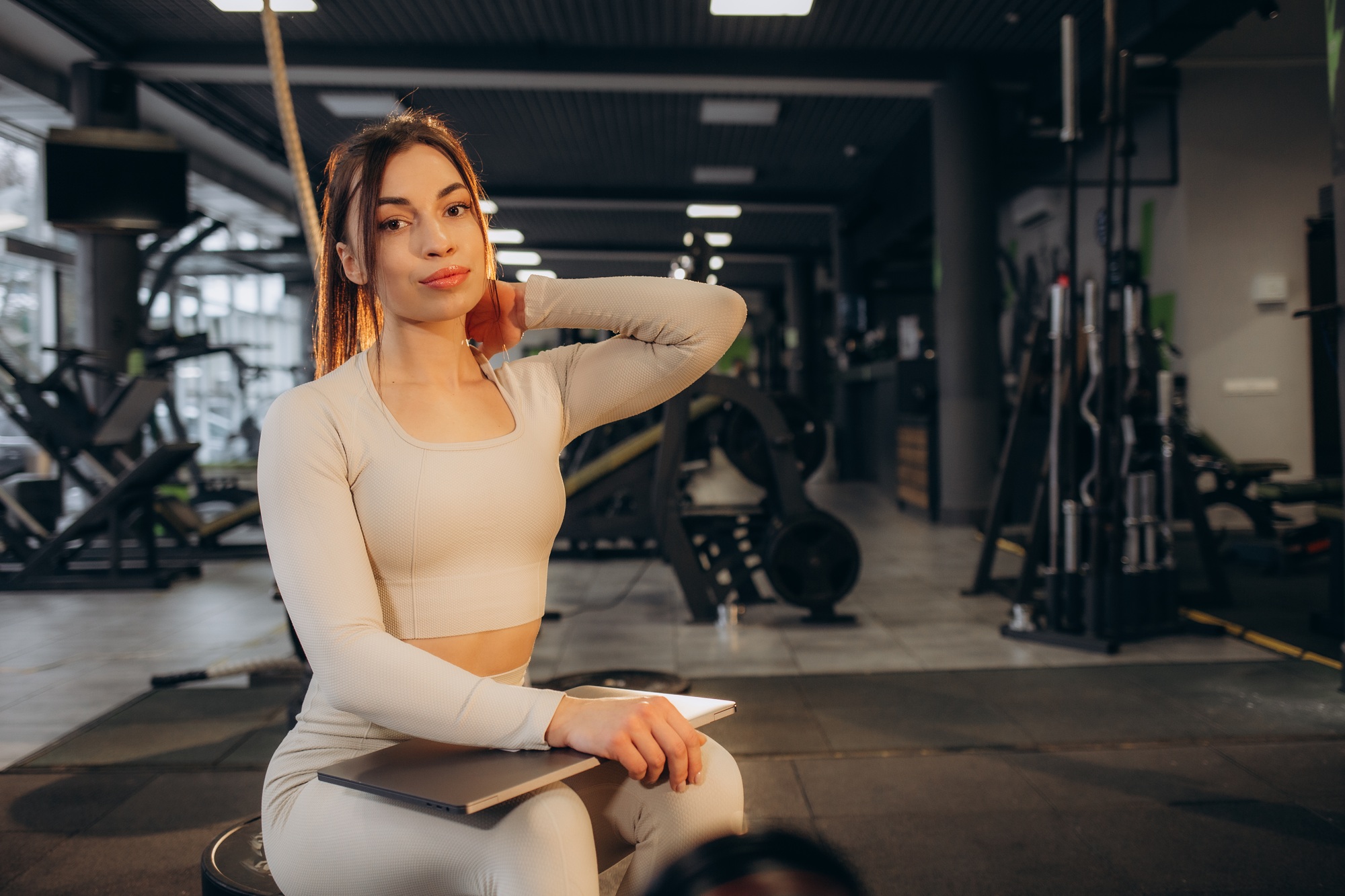 A woman with a laptop sits in the gym. Online training