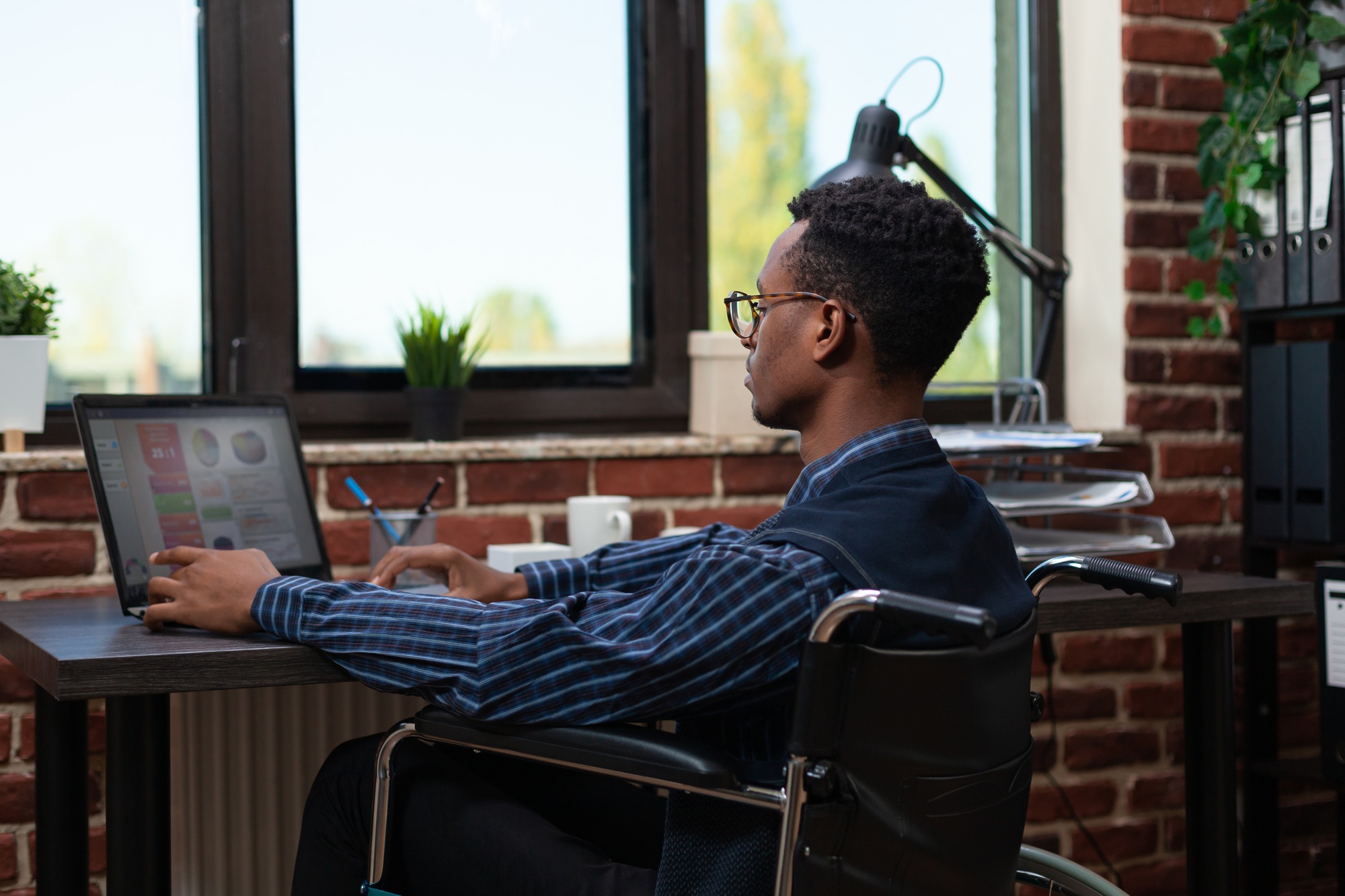African american employee who is paralyzed analyzing key performance indicators on laptop