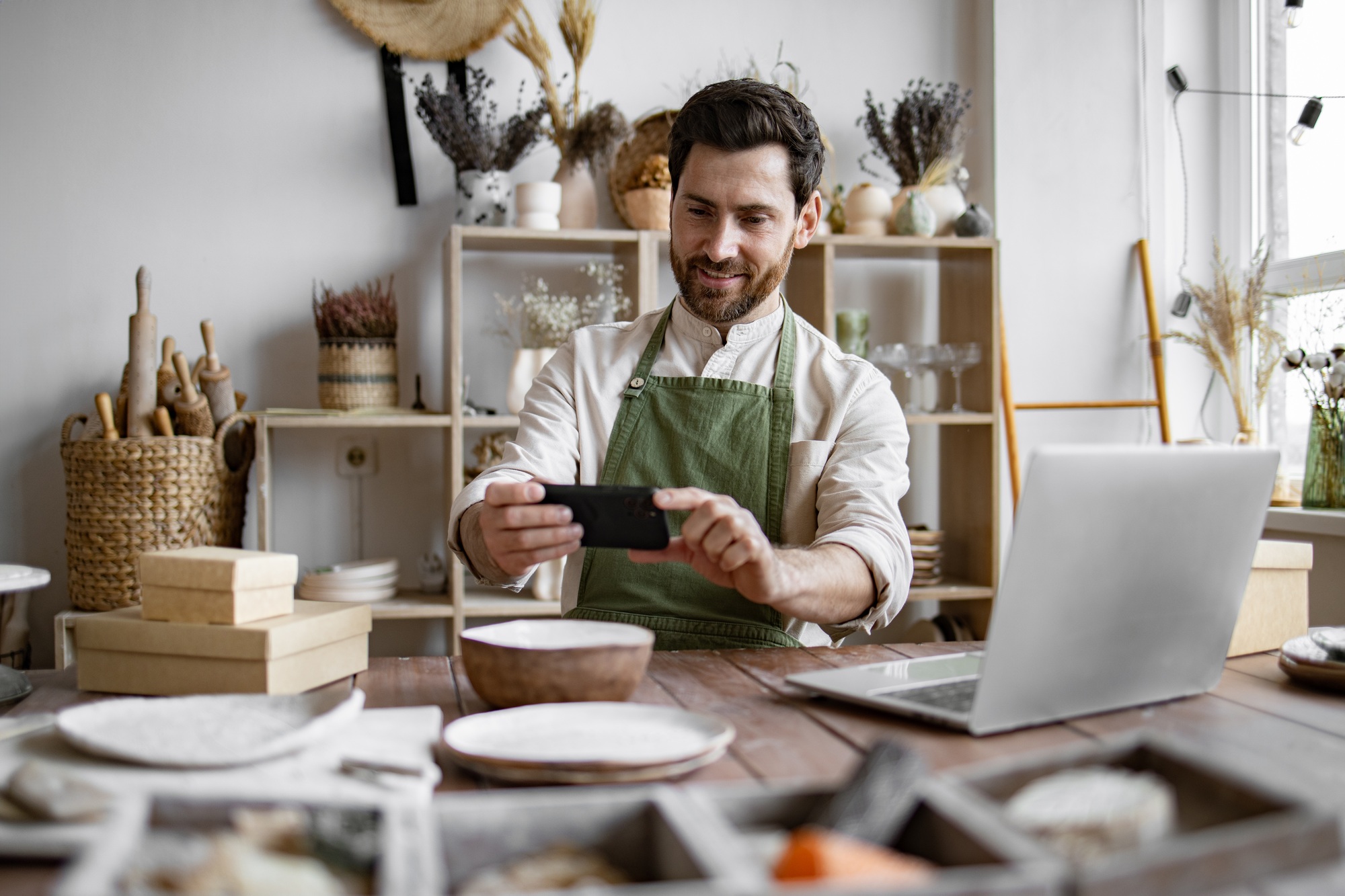 Bearded mature man potter takes photos of handmade bowl from clay.