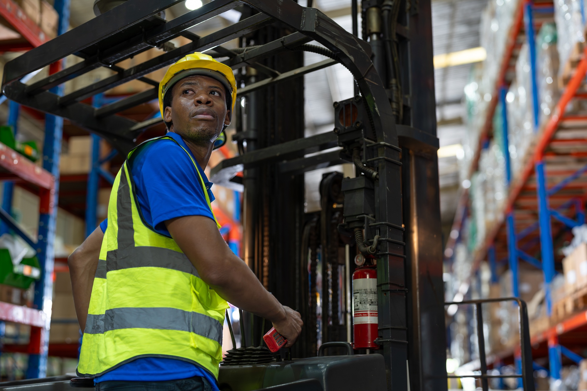 Black man employee driving forklift unload and moving goods for retail warehouse shipping.