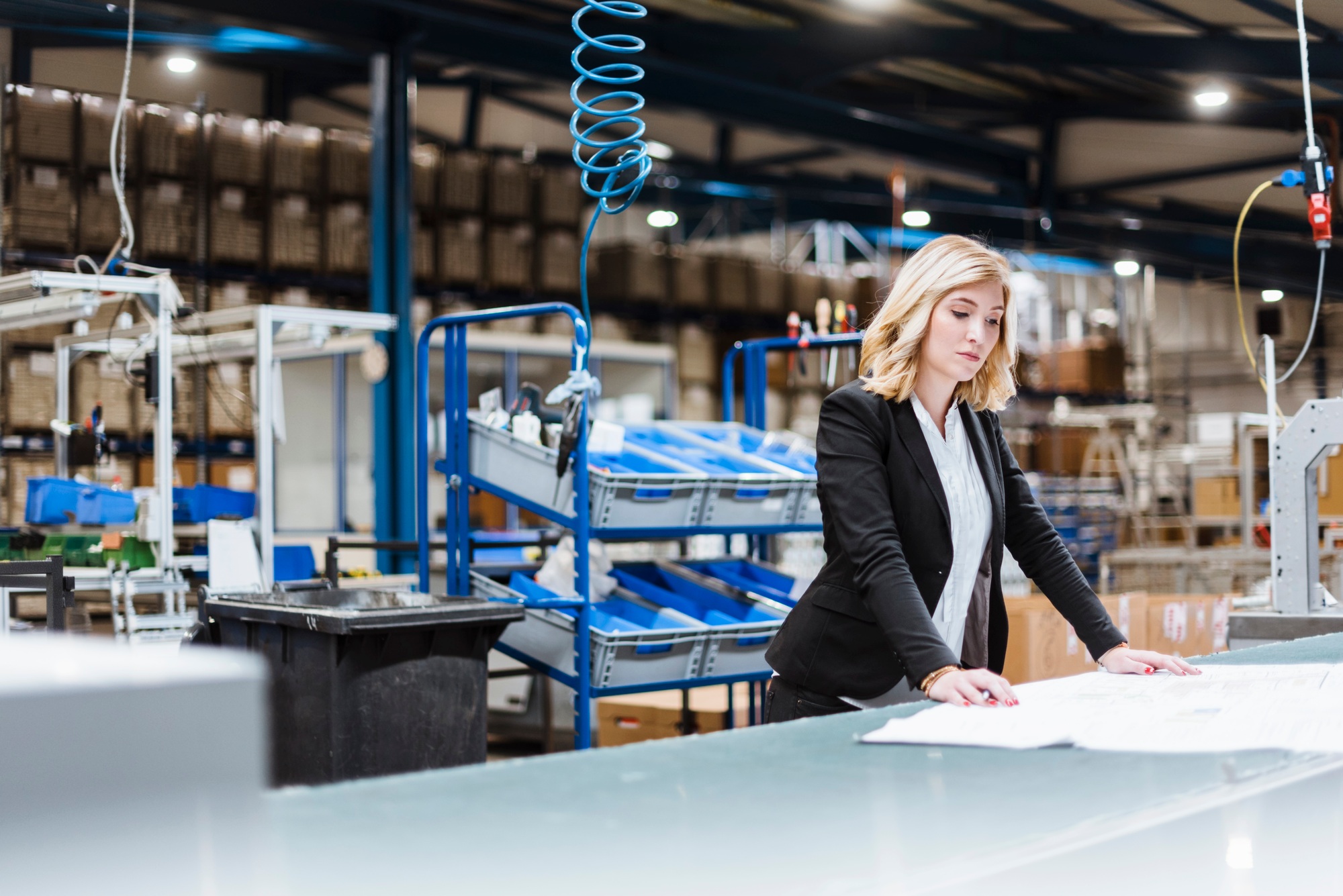 Blond businesswoman standing on shop floor, looking at plans