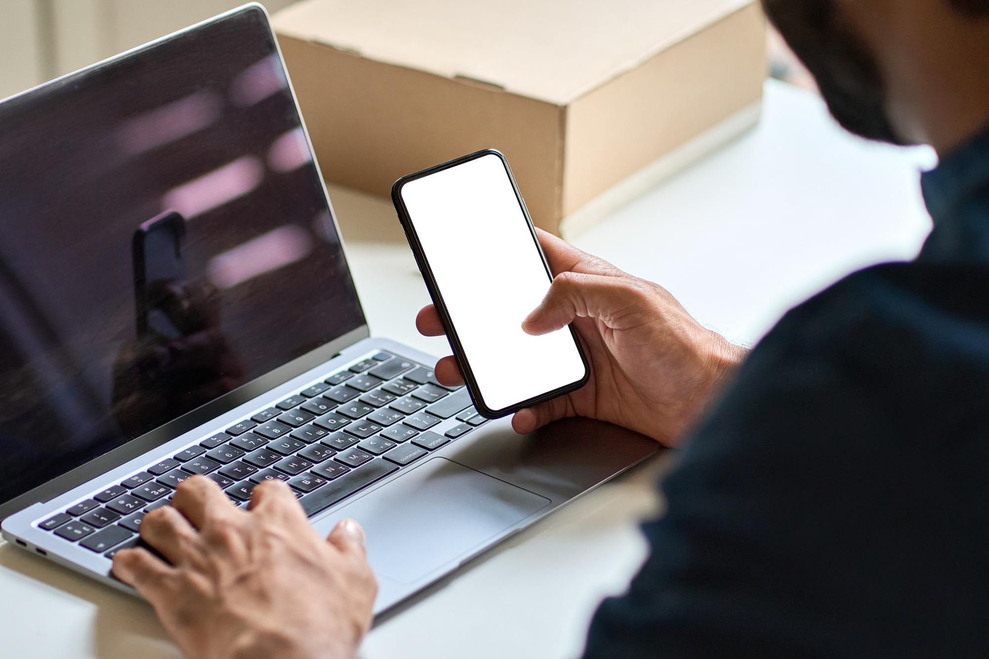 Business man holding smartphone with mock up screen at work desk.