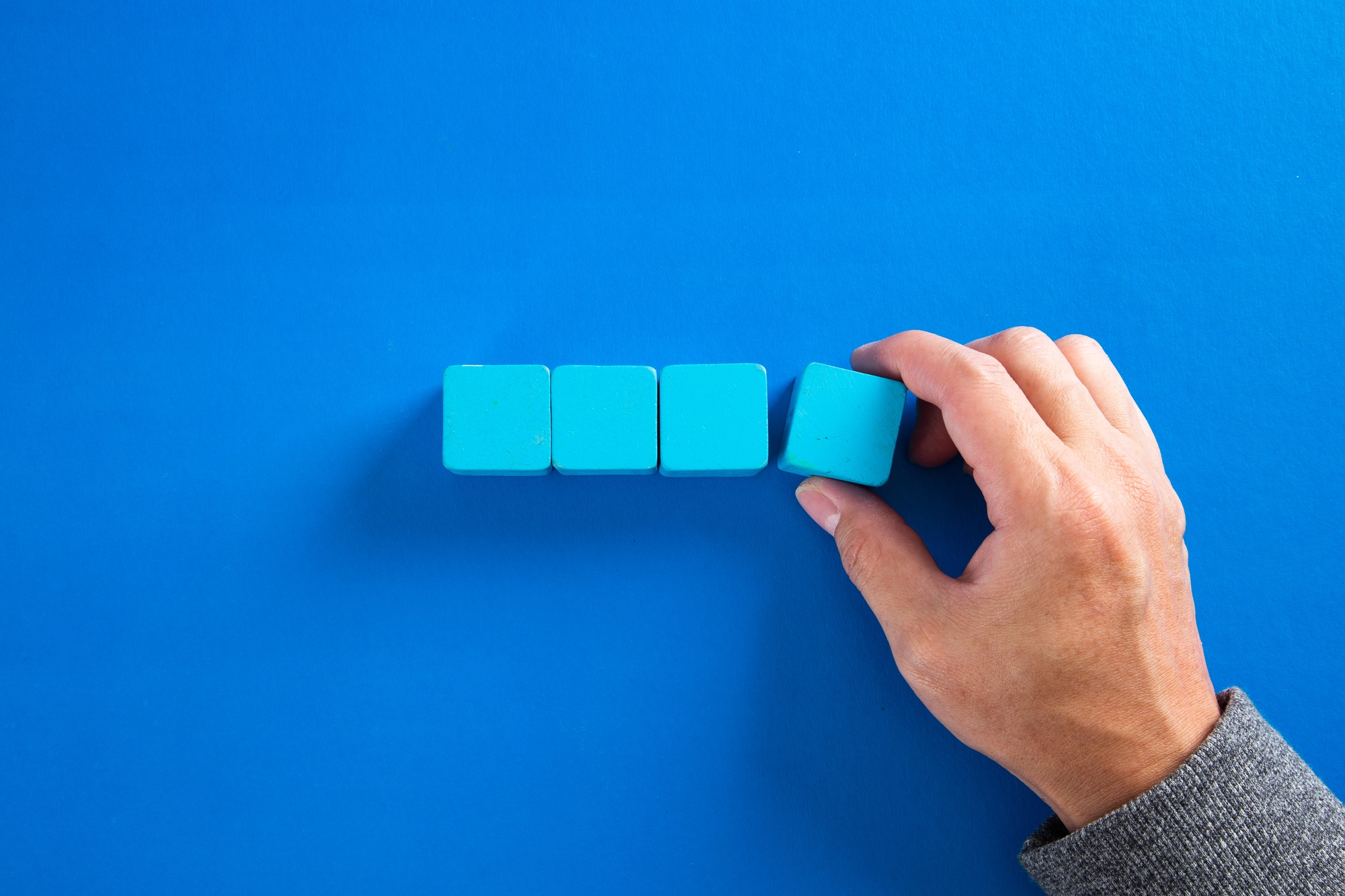 Businessman building a structure with four blue toy blocks on blue background