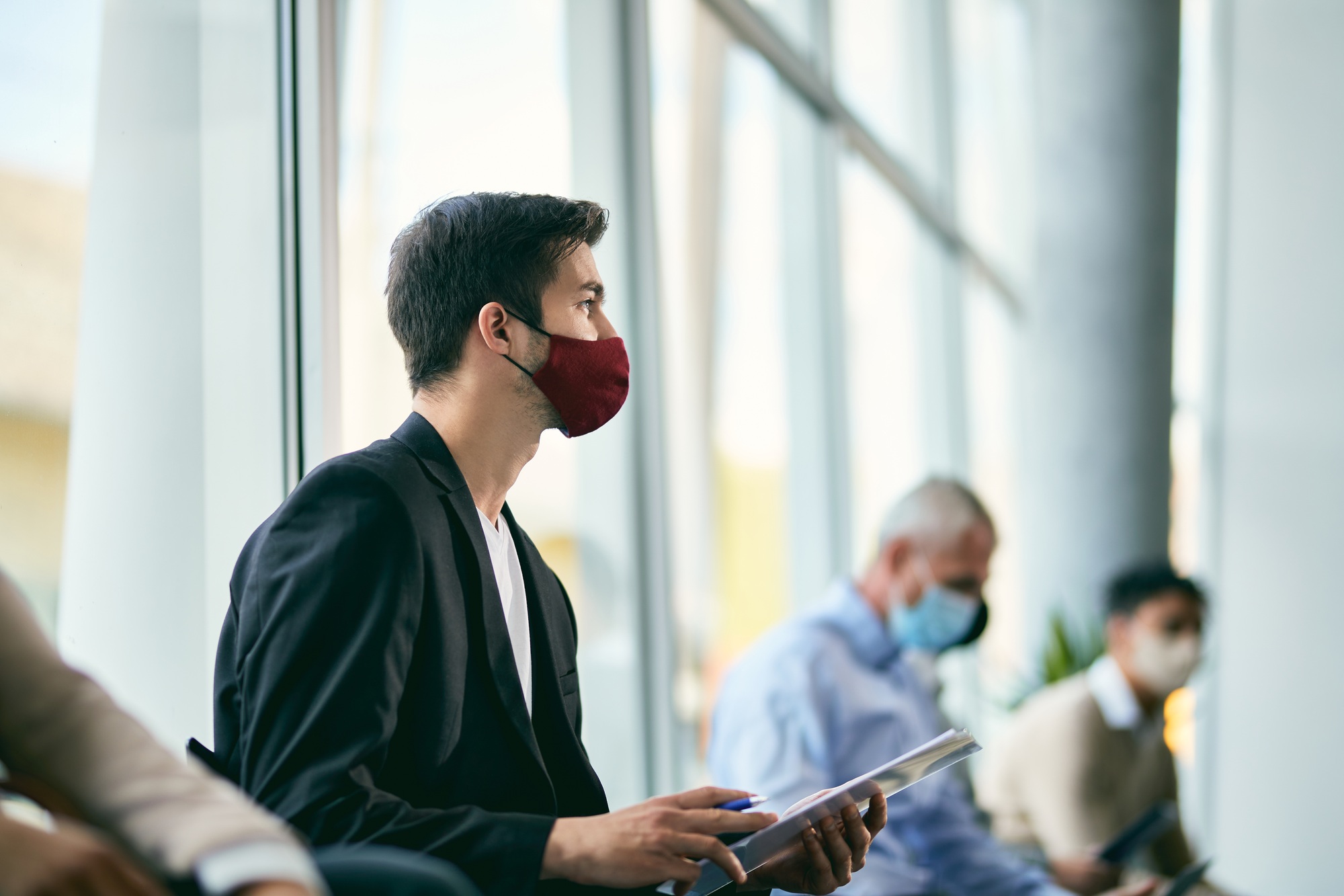 Businessman with face mask employment documents while sitting in waiting room of an office building.