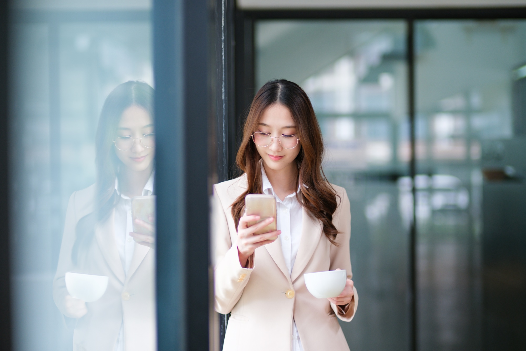 Businesswoman smiling while holding a coffee cup and checking her phone during a work break