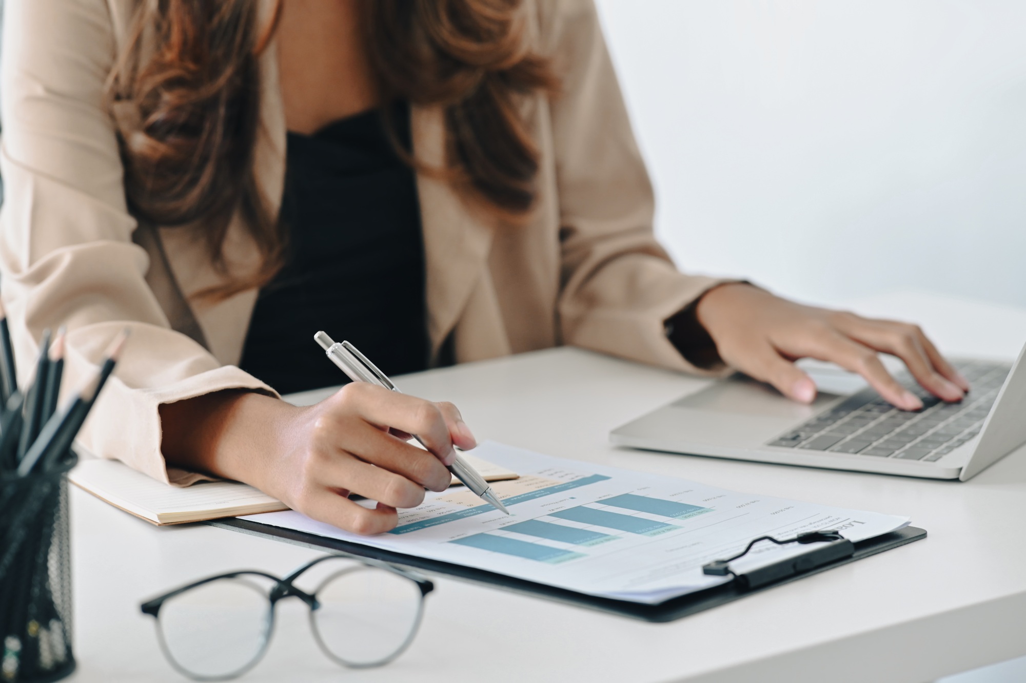 Businesswoman typing on laptop and writing information on document.
