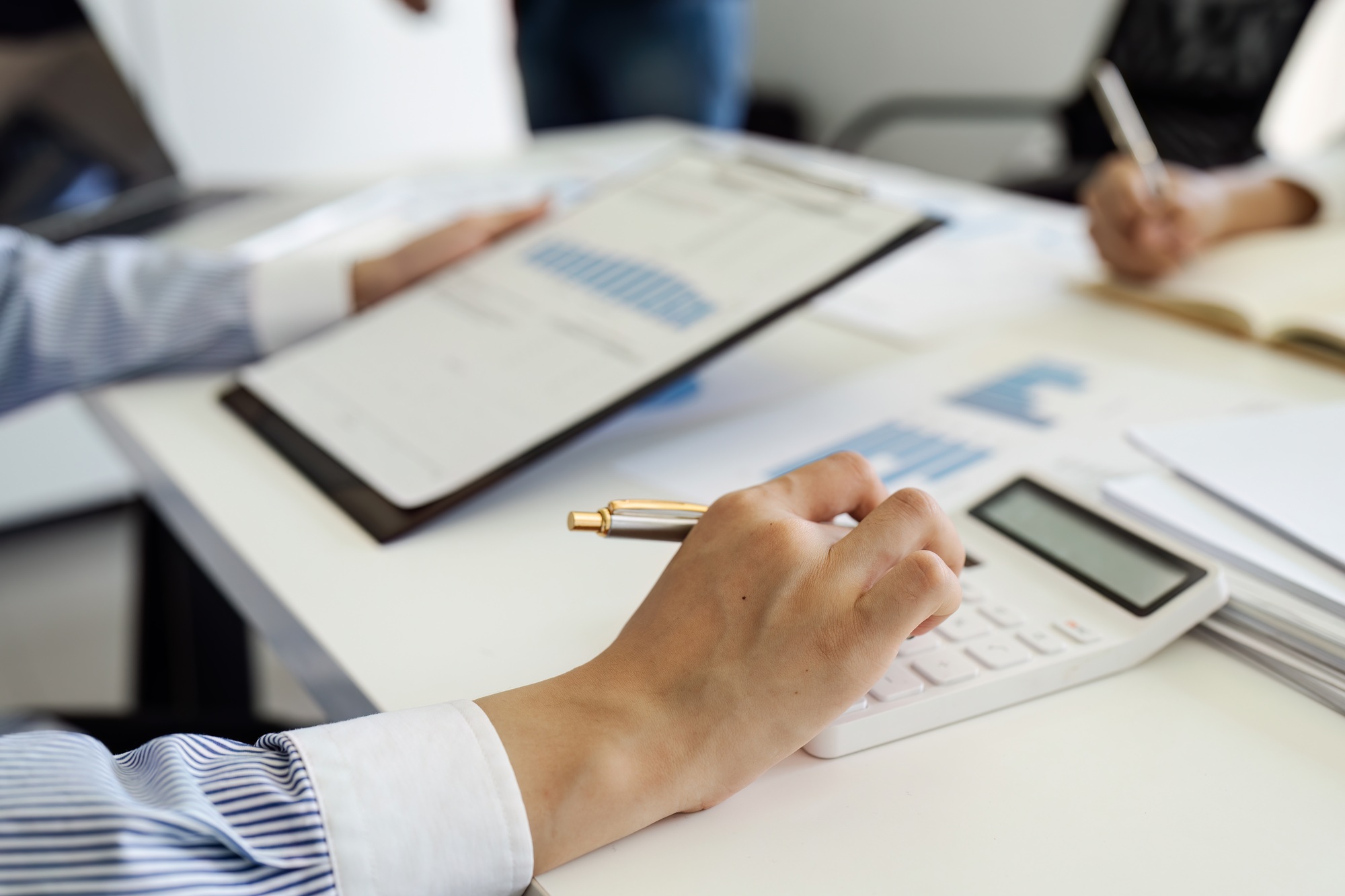 Businesswoman using a calculator to calculate numbers on a company's financial documents, she is