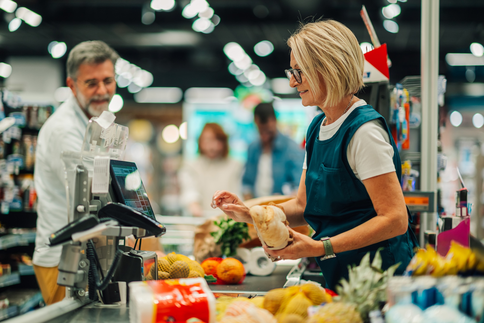 Cashier scanning groceries at checkout with customer waiting in supermarket