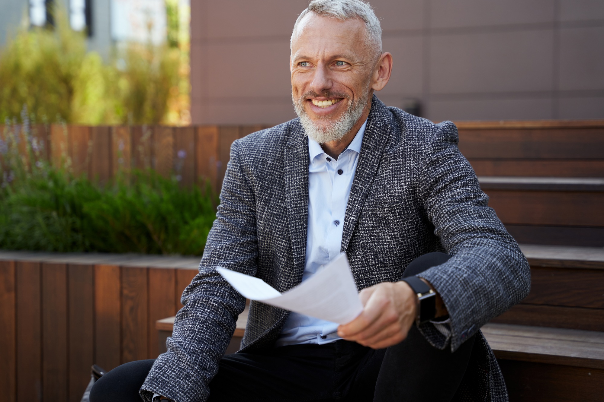 Cheerful elegant mature businessman holding papers, reading financial statistics while sitting