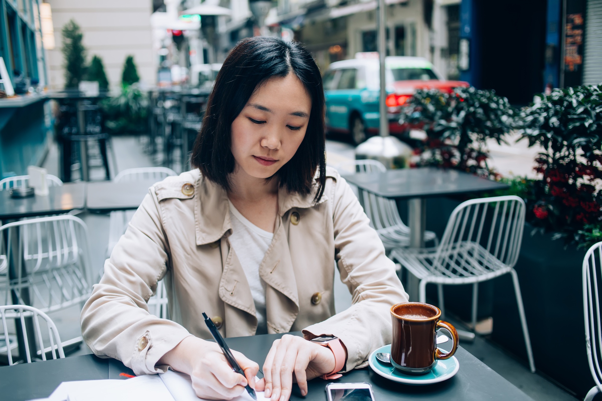 Content modern Asian woman writing in planner at street cafe