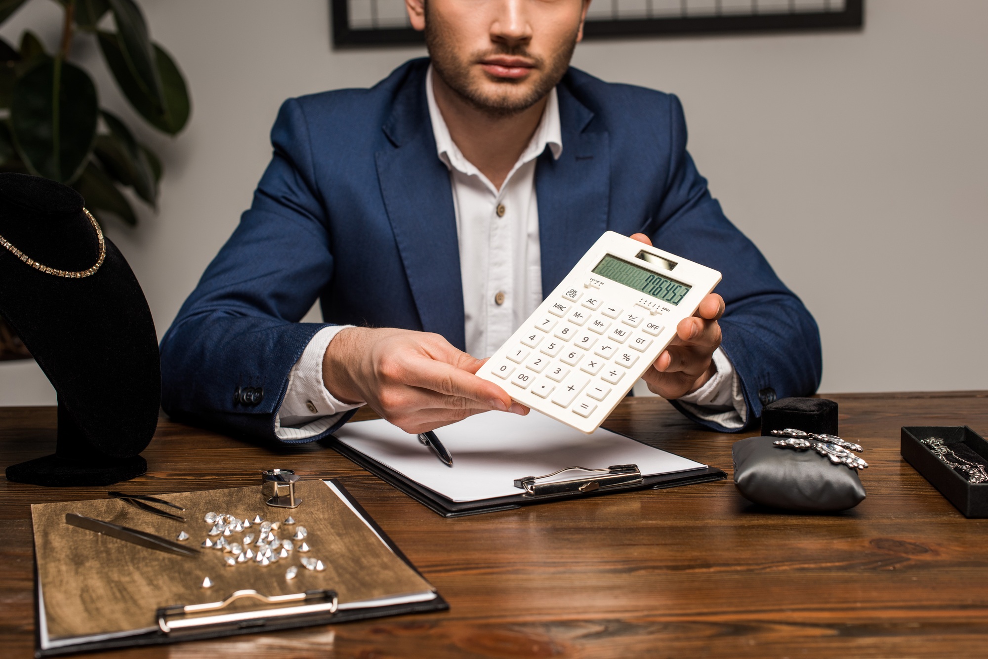 Cropped view of jewelry appraiser showing calculator near clipboard and jewelry on table