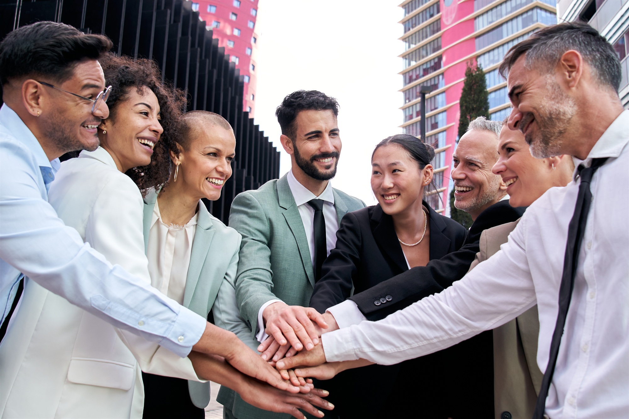 Diverse excited business team in suits joining hands in community. Fellowship, positive relationship