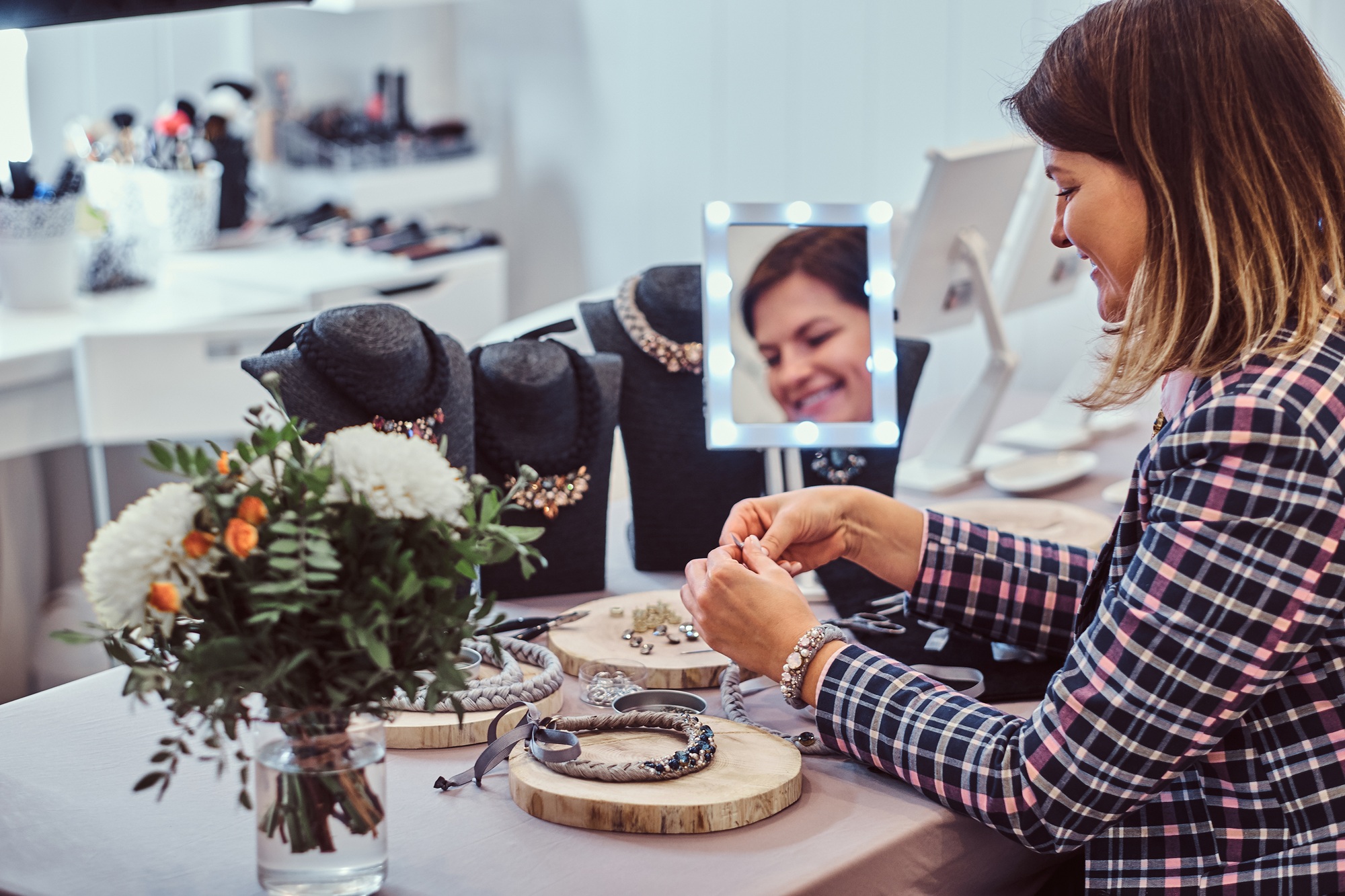 Elegantly dressed woman makes handmade necklaces in jewelry workshop.