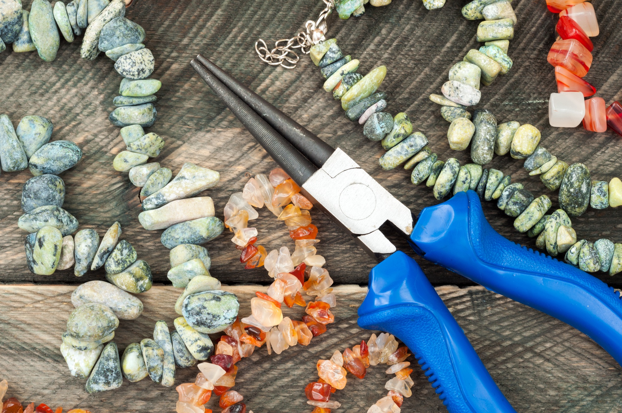 Gems and plier to create hand made jewelry on old wooden background. Handmade accessories