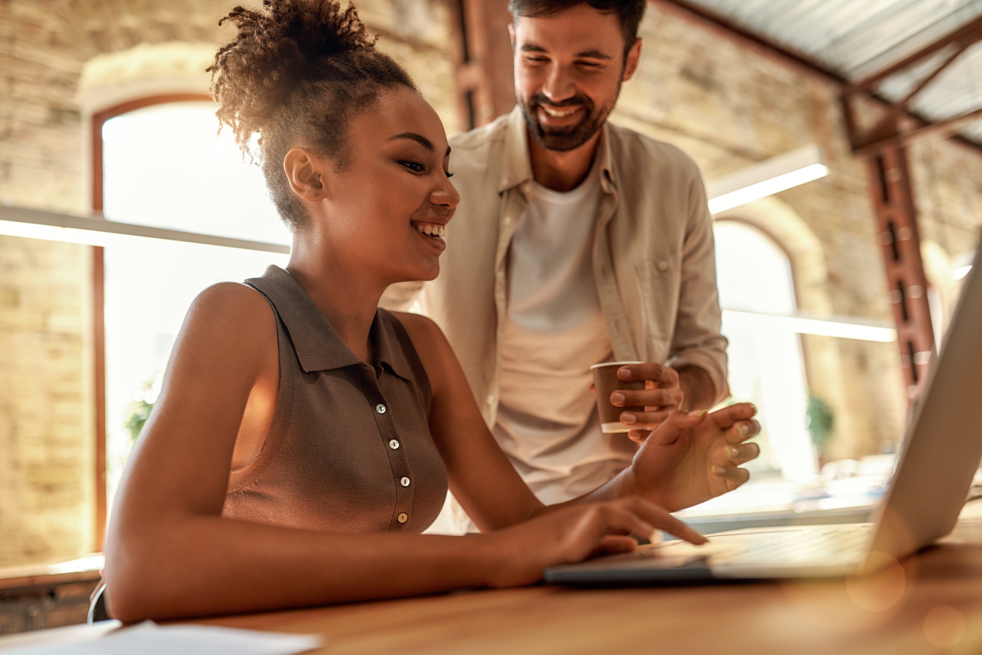 Giving advice. Young and cheerful man holding coffee cup and talking with his colleague while