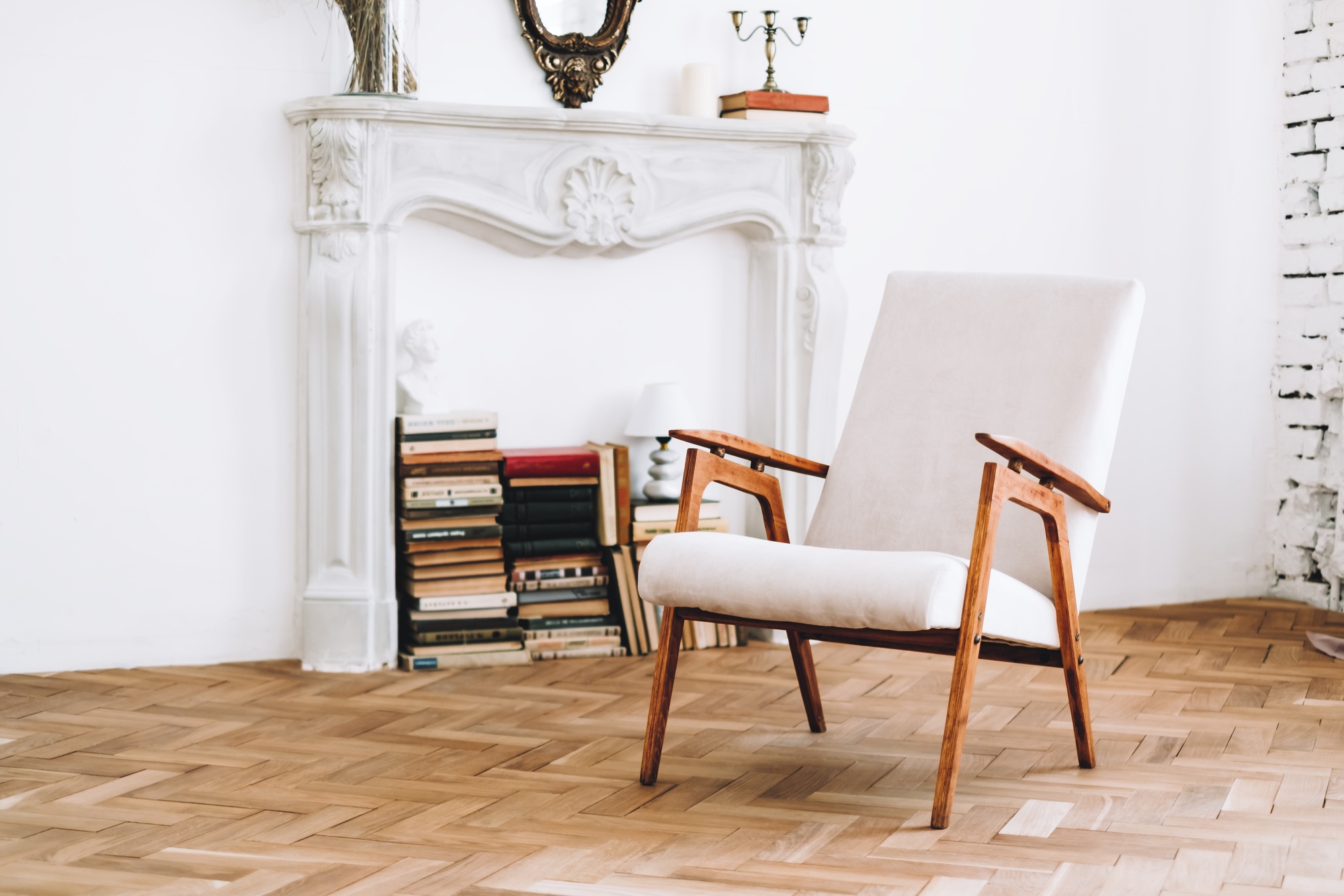 Interior design of stylish living room with vintage white armchair, wooden floor, books, furniture