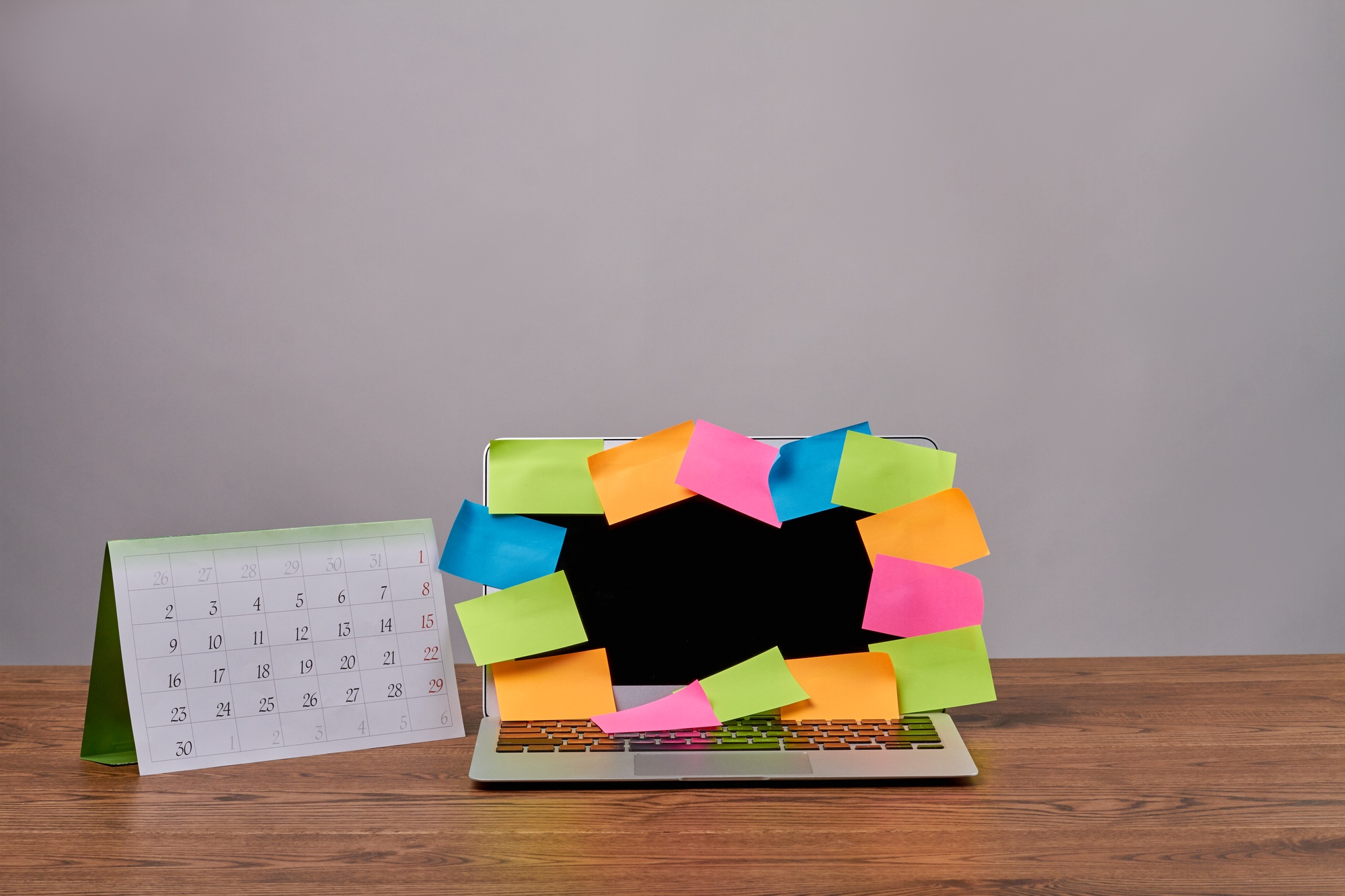 Laptop with colorful sticker notes and calendar on wooden desk.