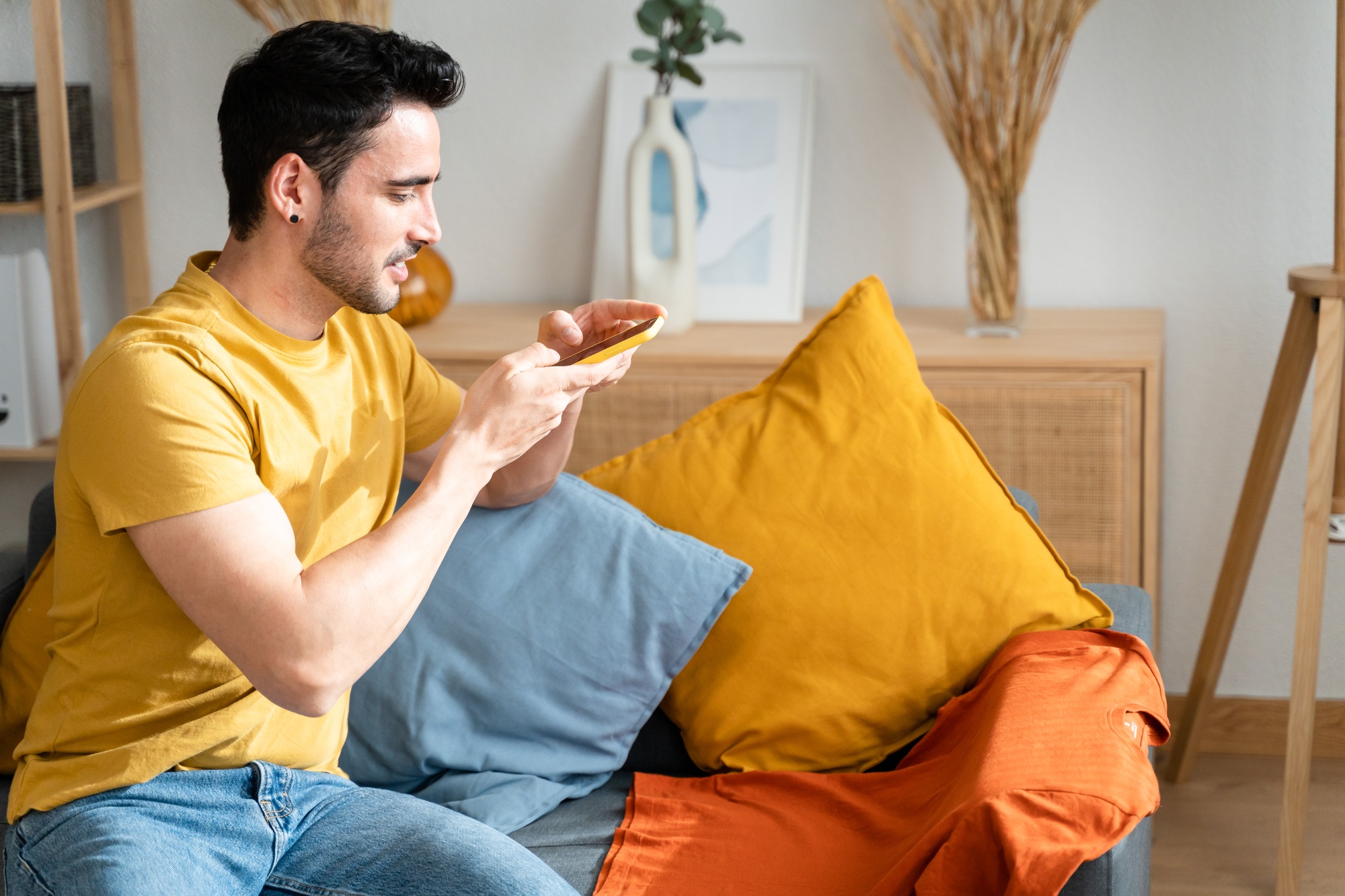 Man sitting on sofa taking a picture of a T-shirt.