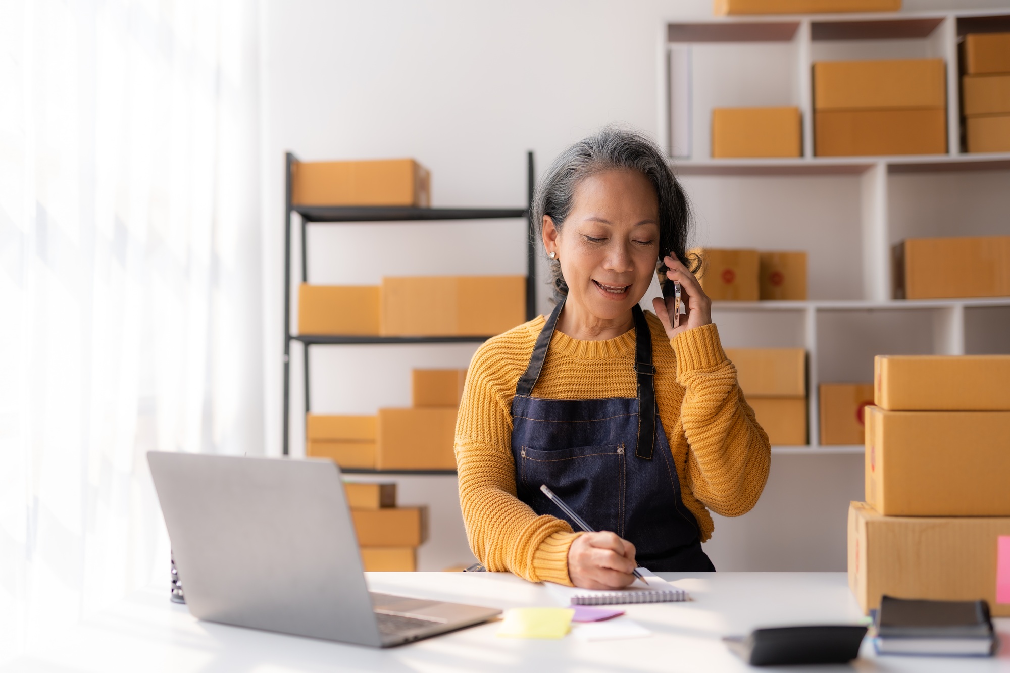 Online owner, Asian senior woman talking on the phone with a customer to track the delivery.
