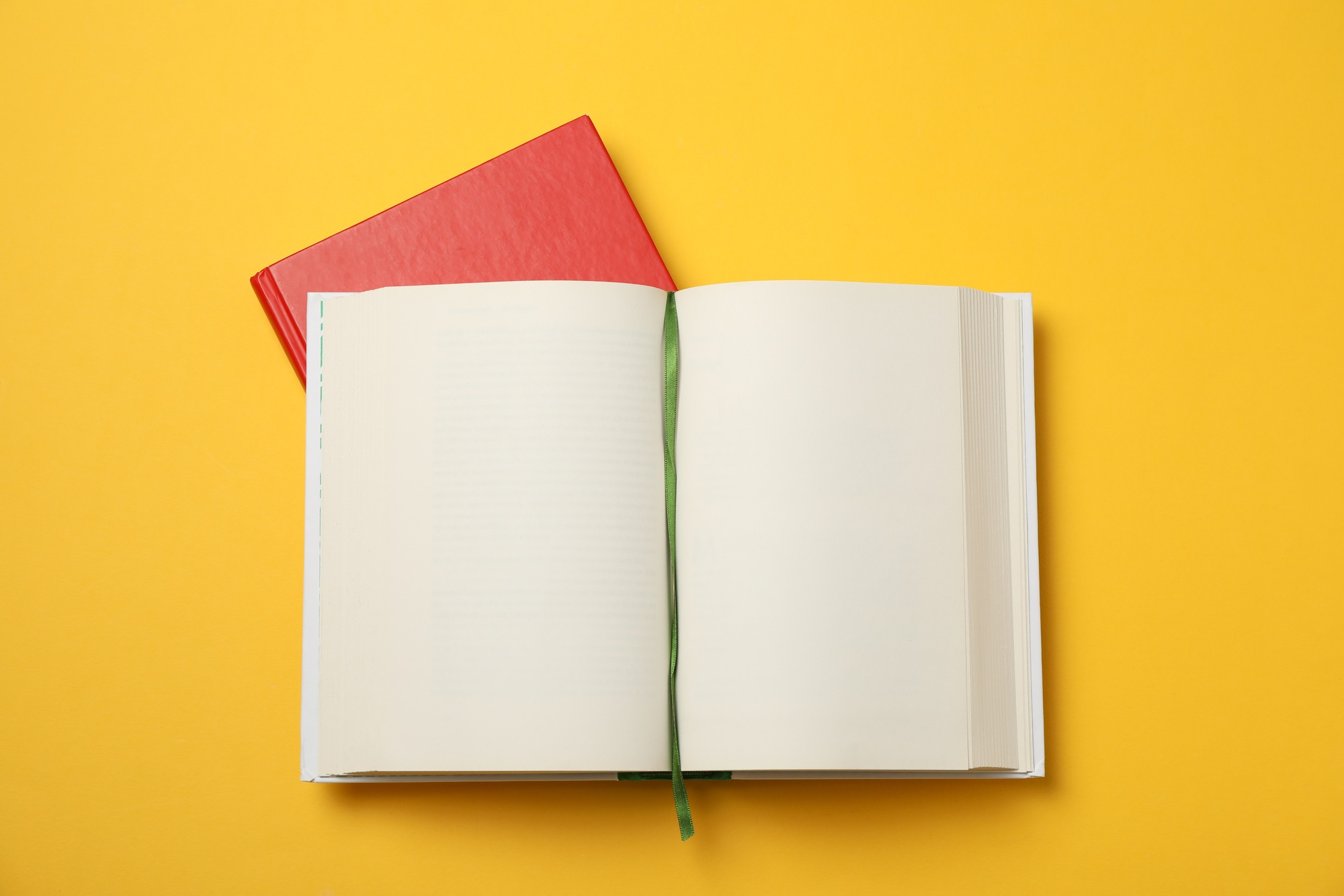 Opened empty book and red book on yellow background, space for text