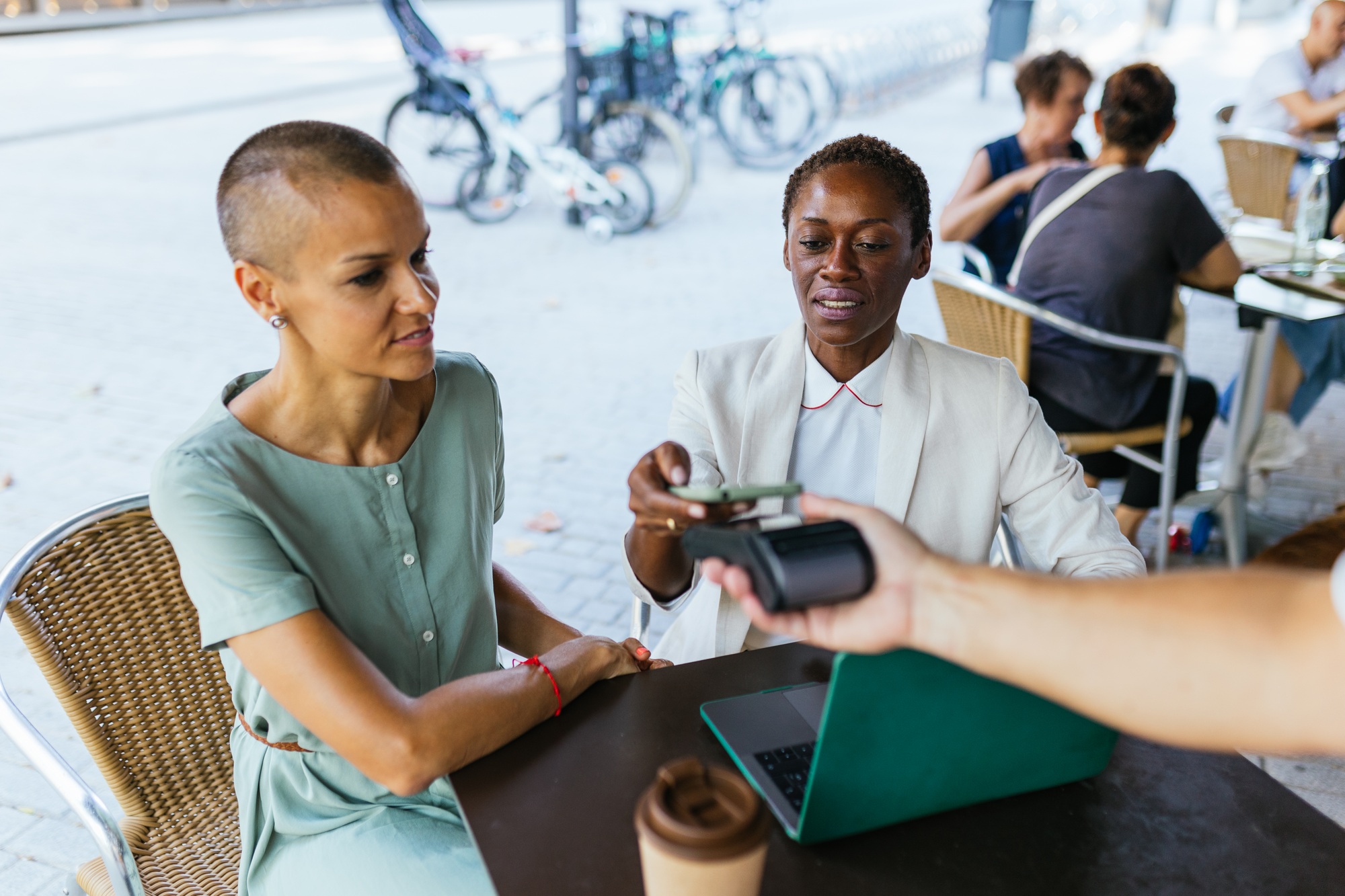 photo of two businesswomen, paying the bill with their mobile phones at a POS. on the terrace of a