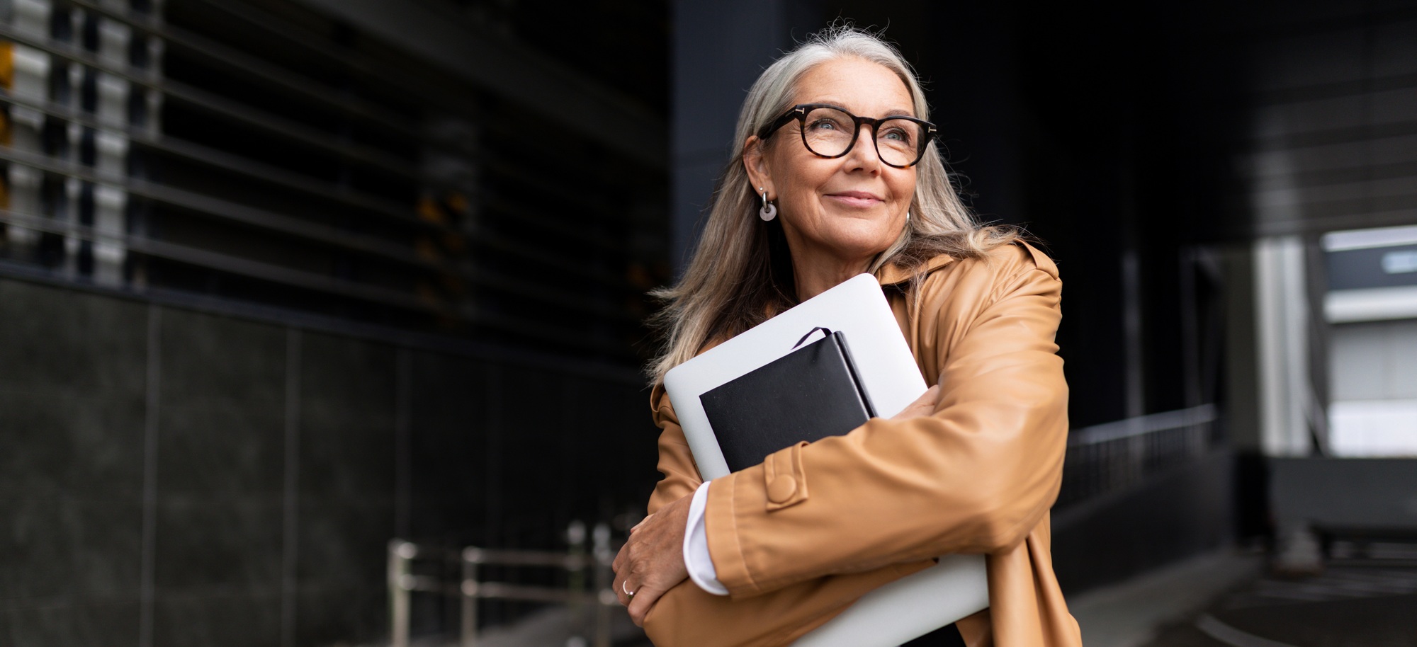 portrait of an elderly businesswoman with a laptop in glasses outside the office, strong and