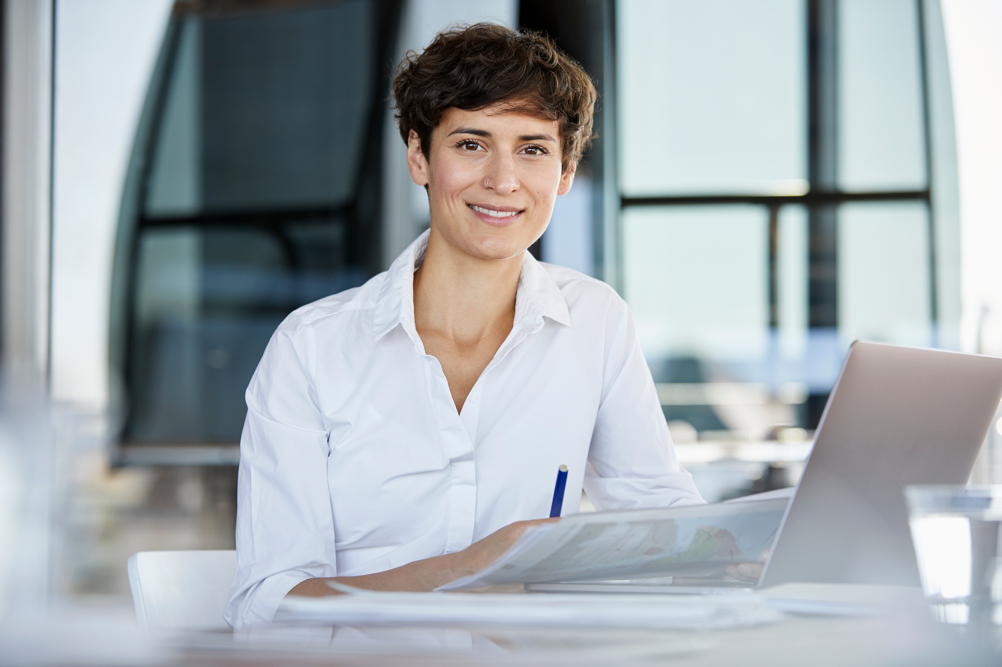 Portrait of confident businesswoman sitting at desk in office with laptop and document