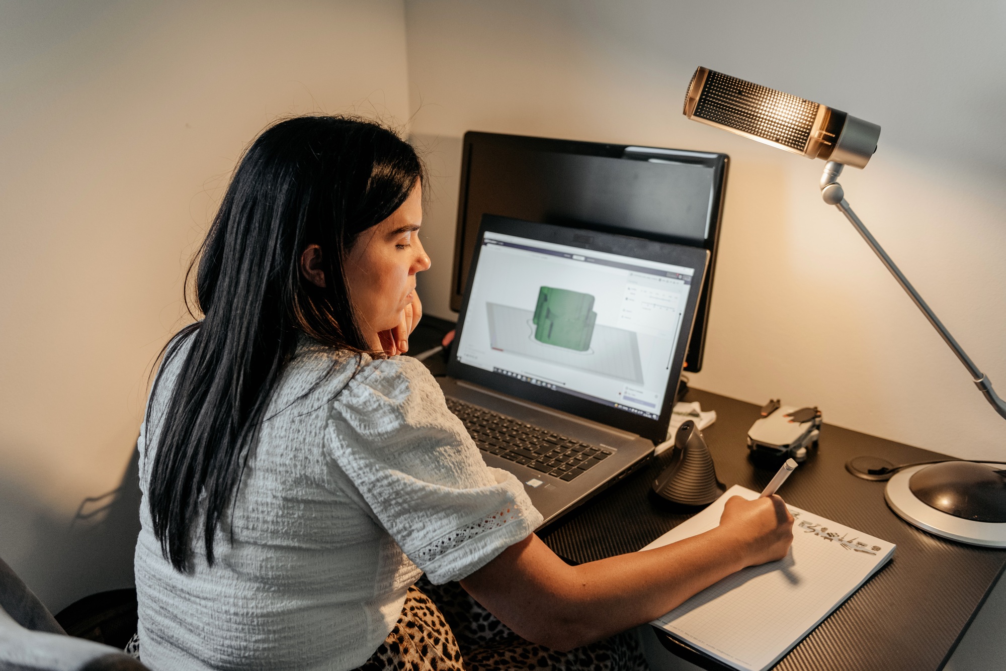 Rear view of young businesswoman sitting at desk, using laptop and 3d design software
