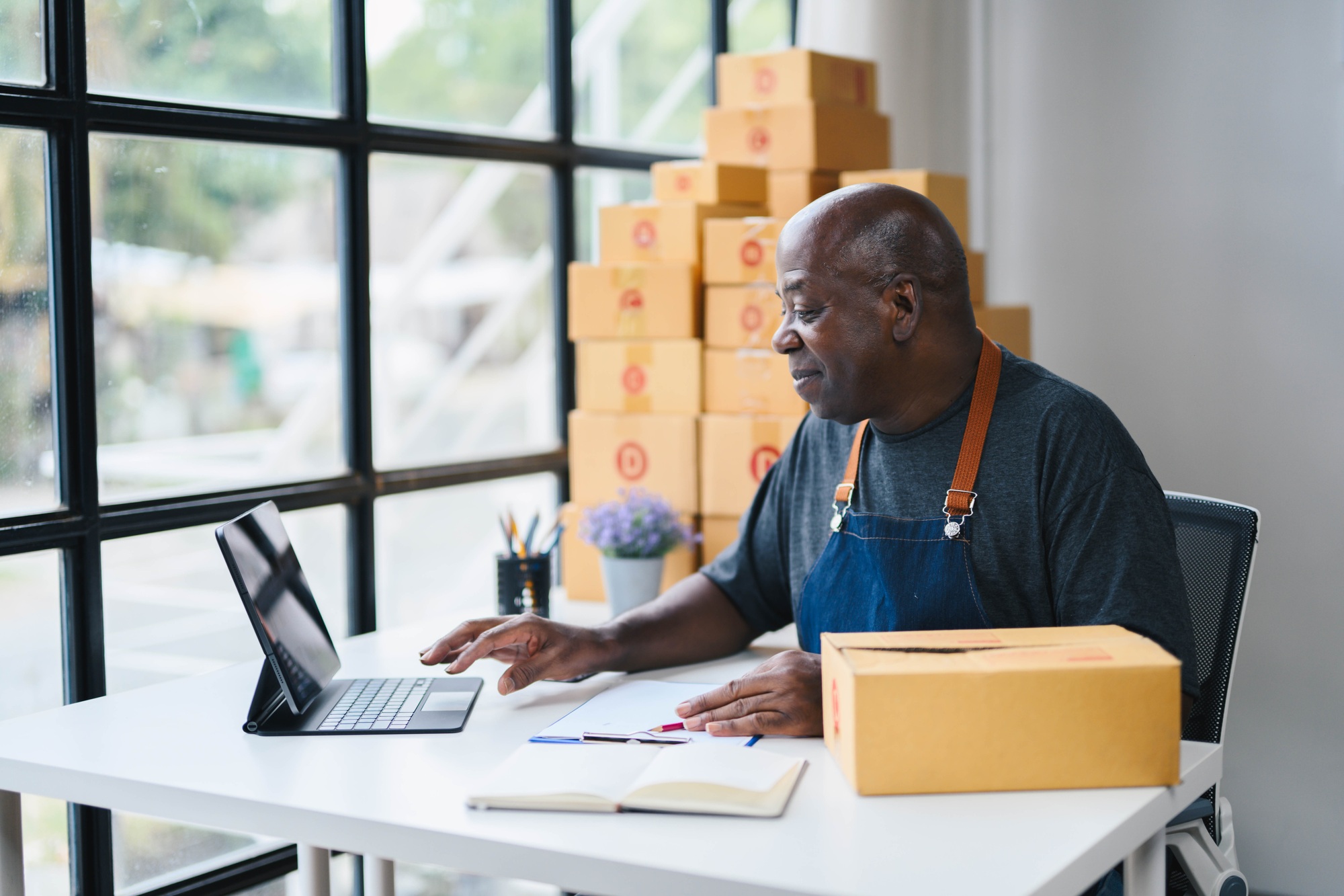 Senior Man Working on Tablet in Home Office with Cardboard Boxes, Small Business Owner, E-commerce