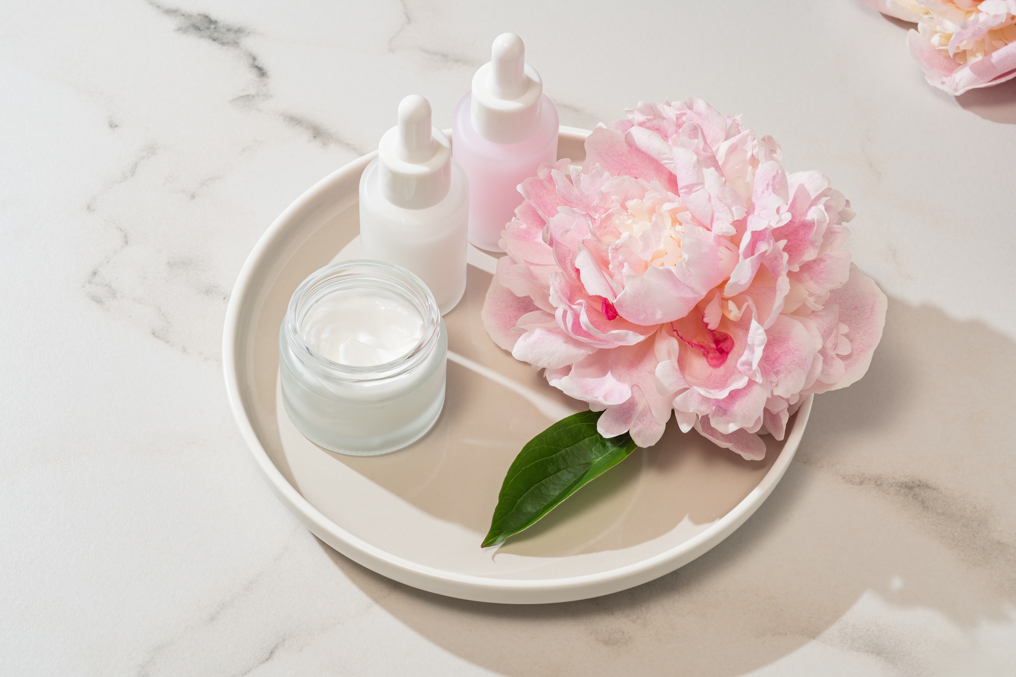 Skincare essentials paired with fresh peony blooms on a tray. botanical beauty meets luxury