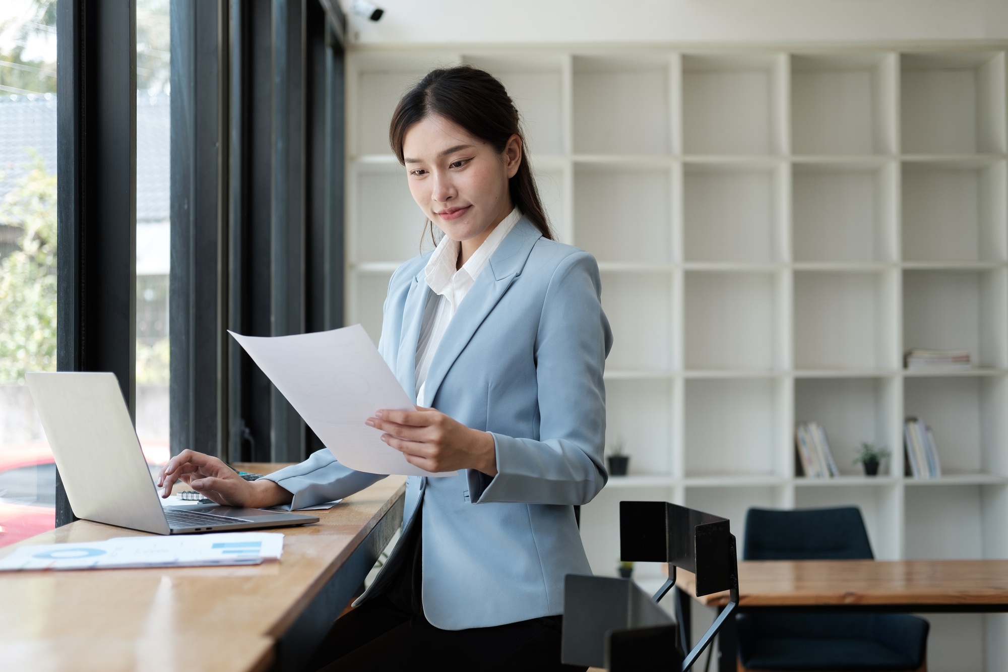 Smart and pretty young Asian businesswoman holding paper, analyzing information from the document, p