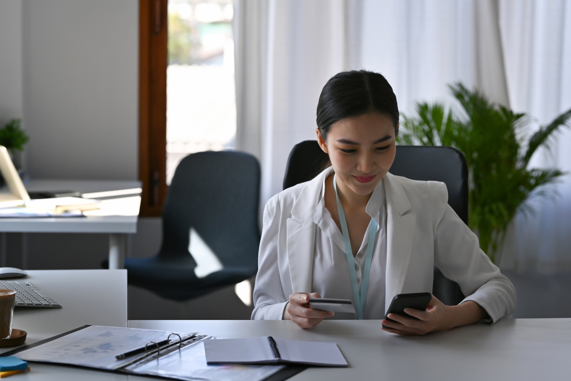 Smiling beautiful businesswoman holding credit card and shopping online with smart phone.