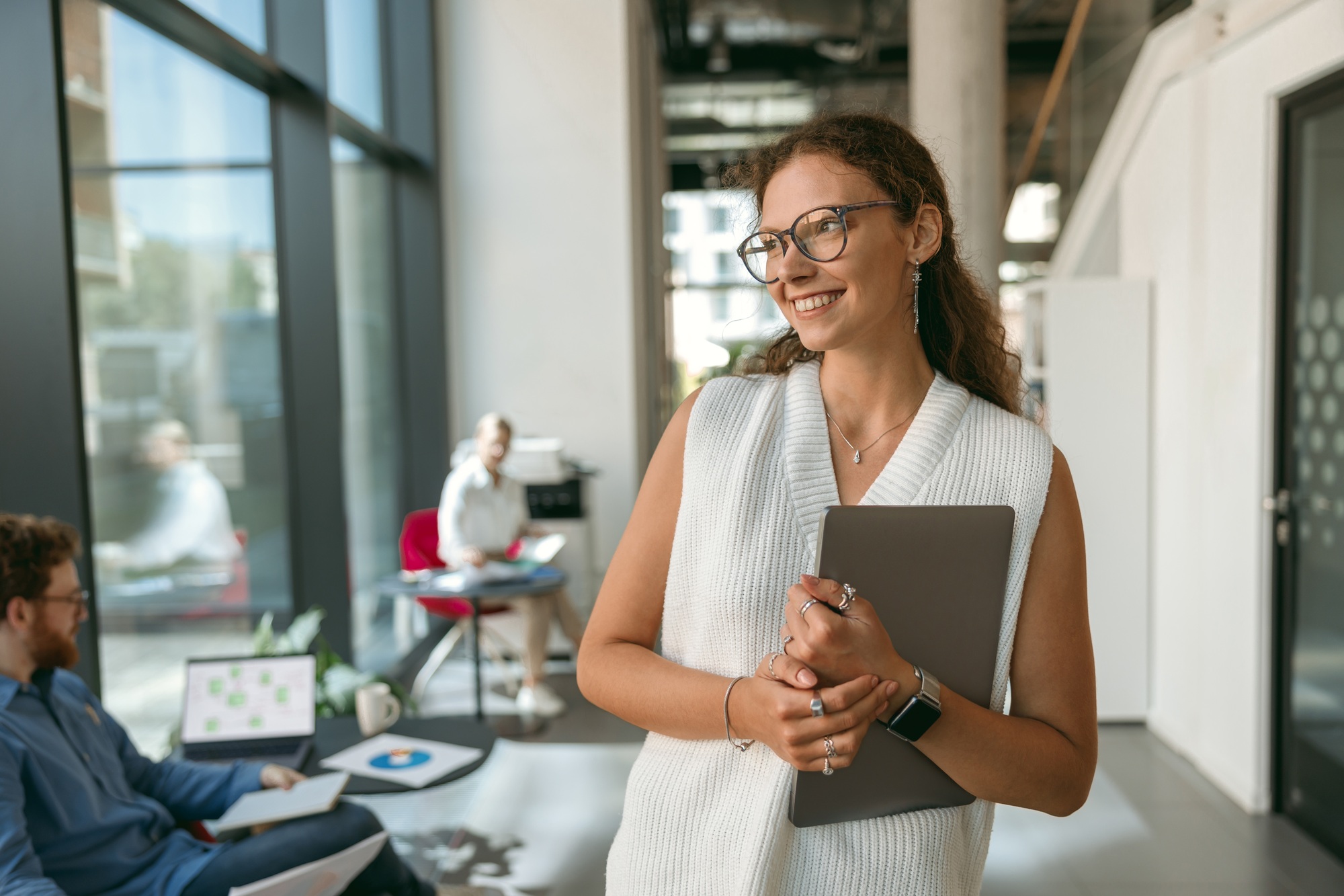 Smiling woman sales manager in eyeglasses with laptop standing in coworking and looks away