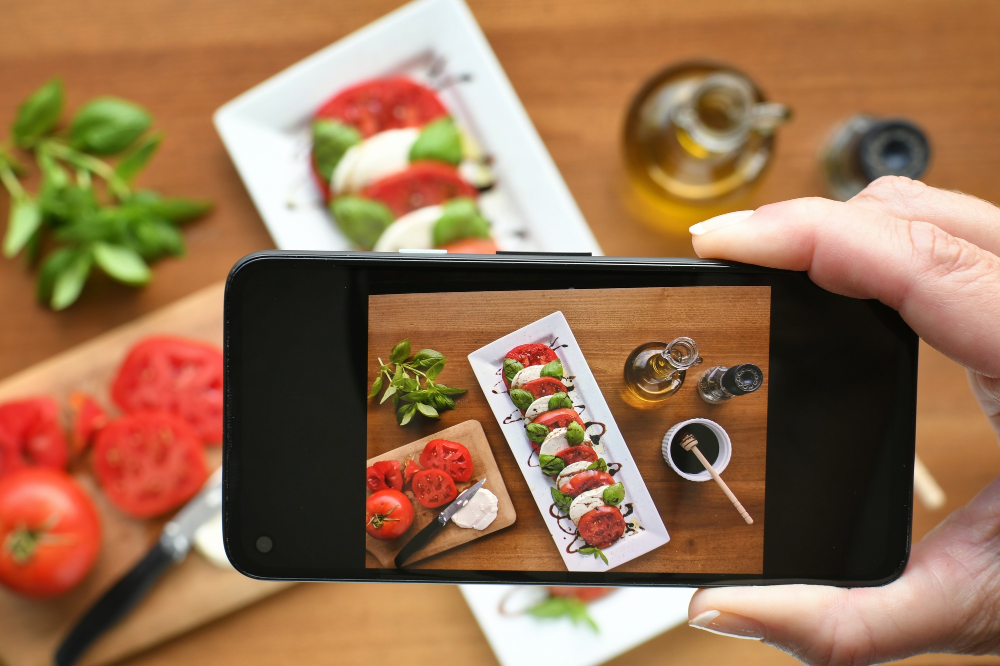 Social media influencer taking photo with smartphone of food, Caprese salad, to post online.