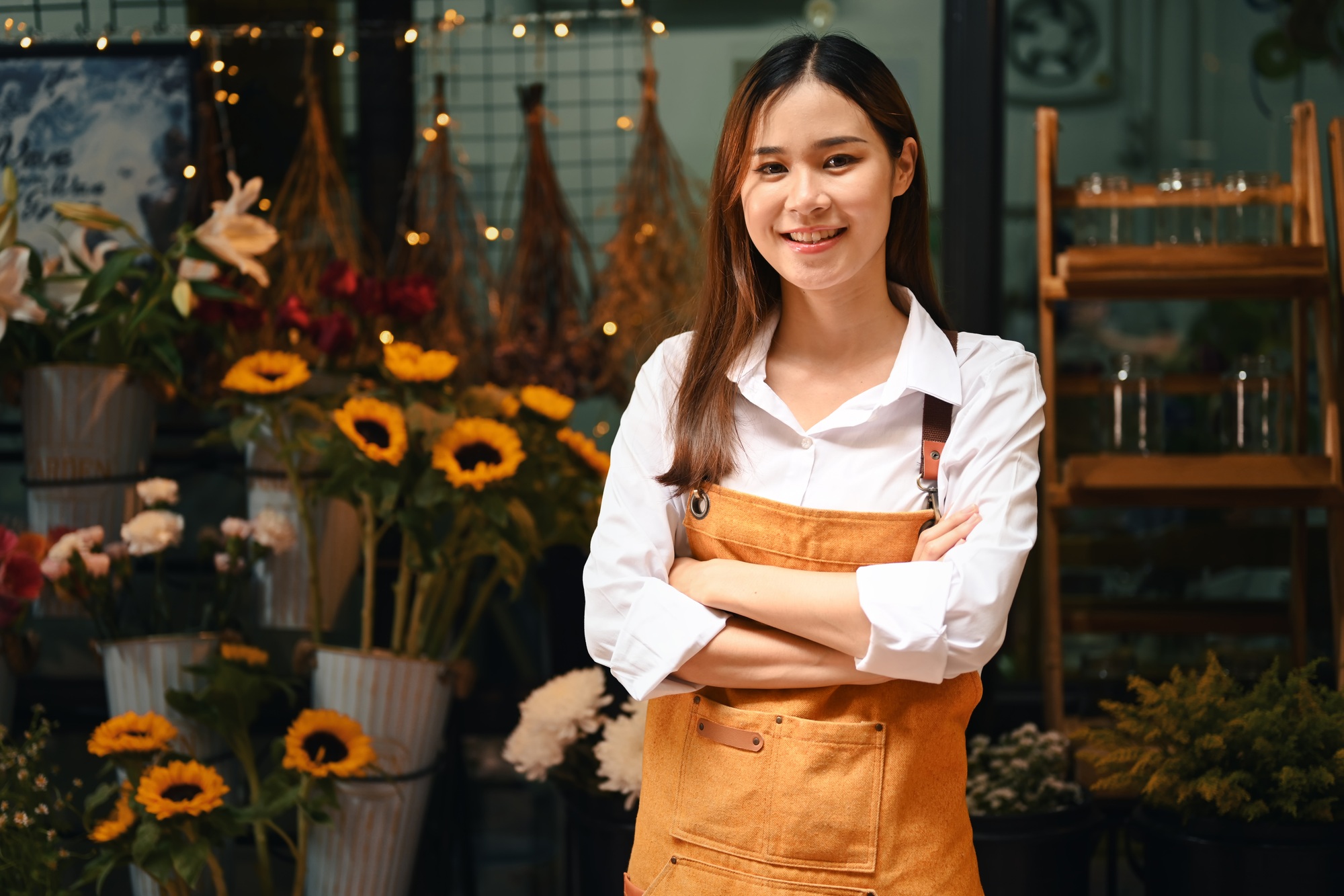 Startup small business entrepreneur in apron standing with arms crossed at her florist shop.