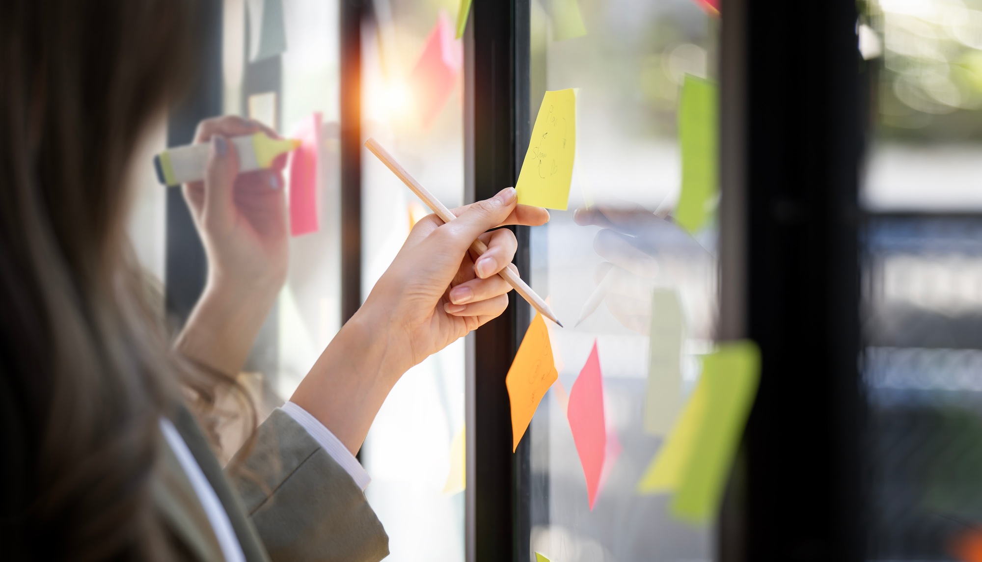 Team or staff discussing with sticky notes a schedule on glass wall for future project together.